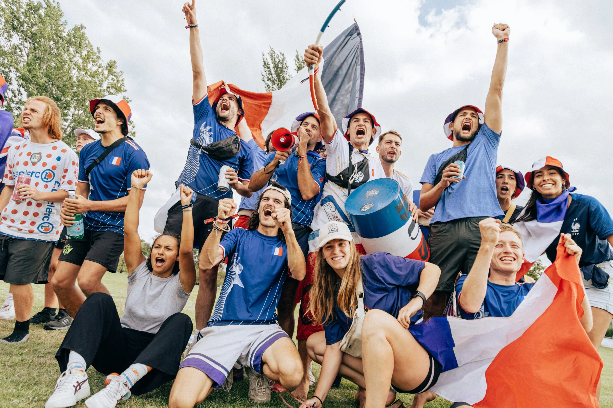 Group of enthusiastic sports fans cheering outdoors, some holding flags and wearing Parisian team apparel.