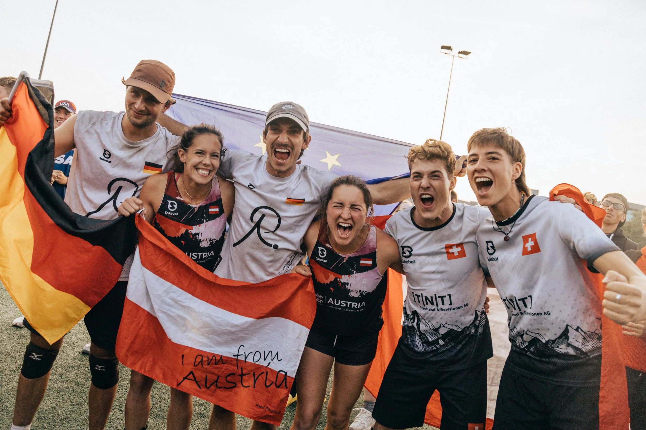 Group of athletes celebrating after a sports event, holding a flag that says "I am from Austria," with a European Union flag in the background.