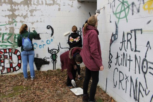 Students armed with paintbrushes and rollers cover over the graffiti covering the Armory's rear walls.