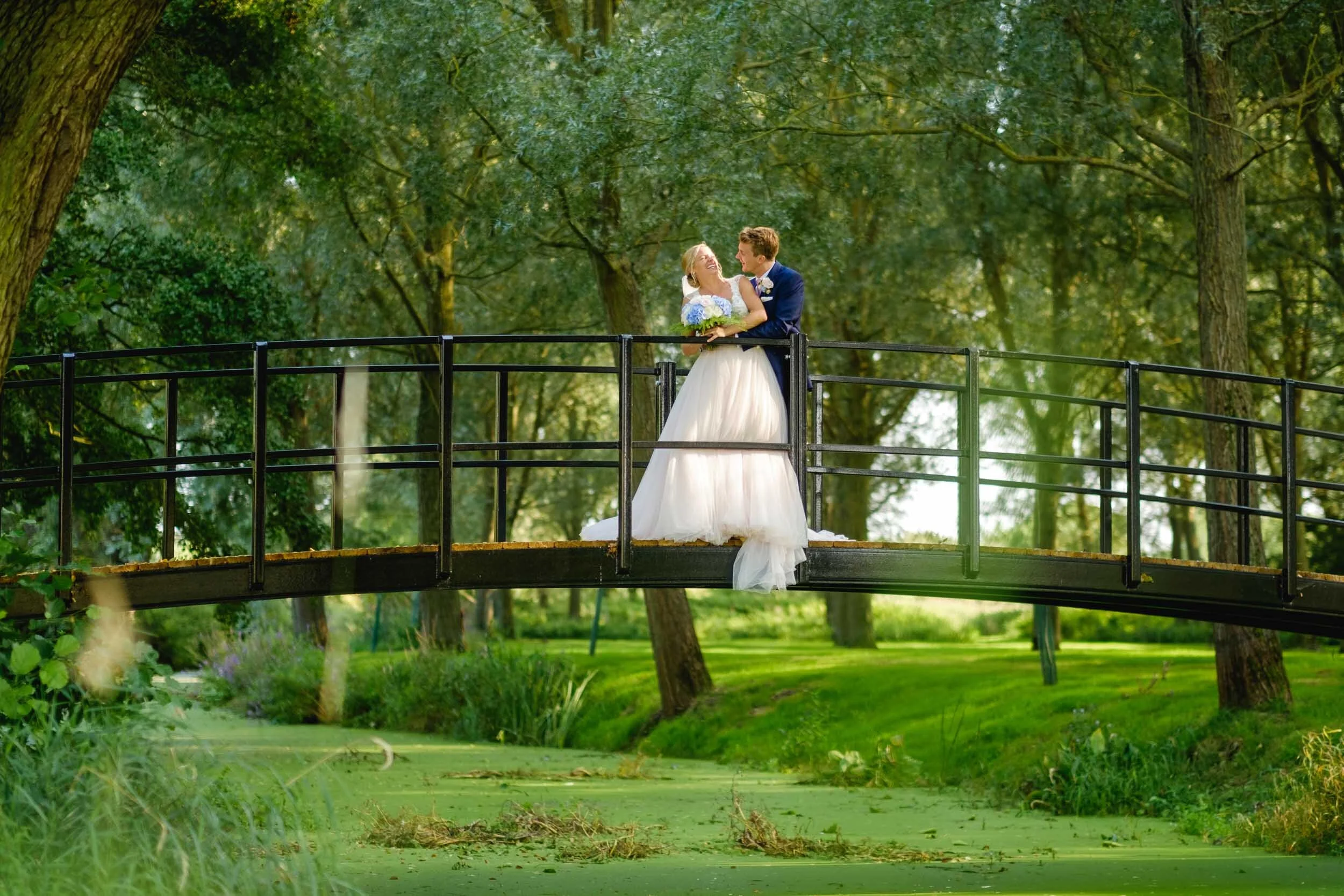 Bride and Groom pose for wedding photographs on the bridge at Suffolk wedding venue Easton Grange