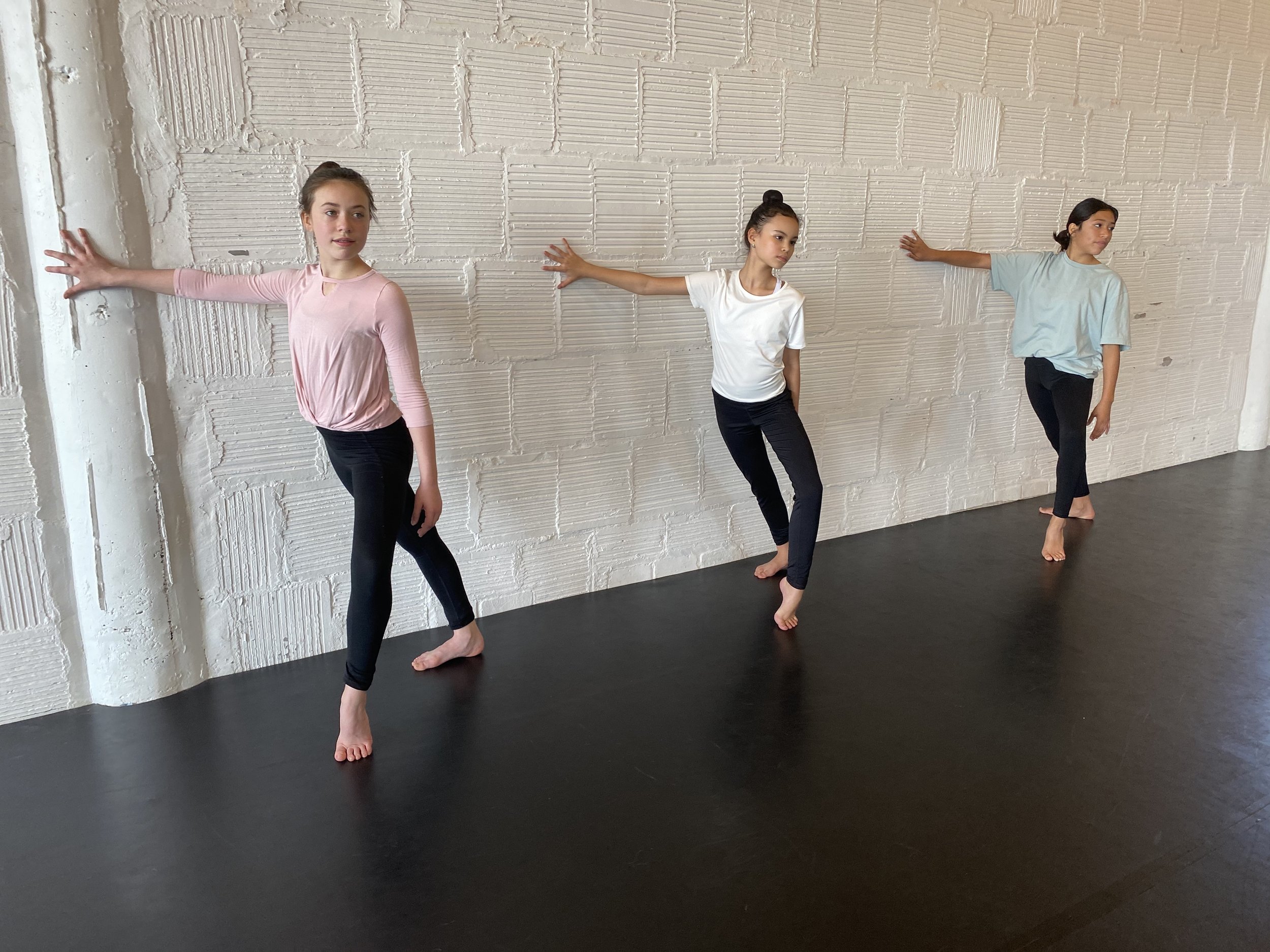 forced arch 3 girls pink white teal shirts black pants hair in buns white brick wall black dance Marley floor Dance acting ballet jazz lyrical contemporary theater musical camp singing voice glee club Amber Keeley director Mpls classes twin cities wo