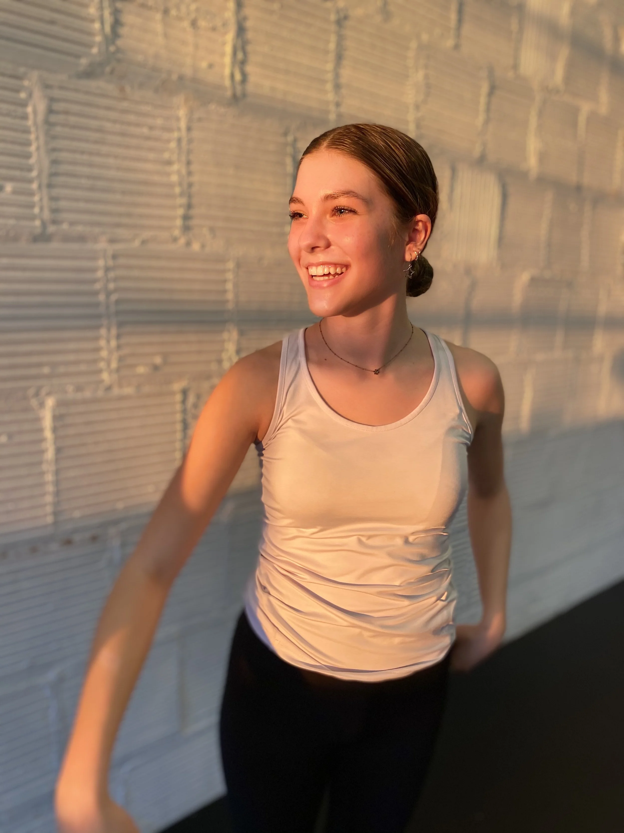 smile laughing white tank top white brick wall golden hour shadow sunset Dance dancer studio acting ballet jazz lyrical contemporary theater musical camp singing voice glee club Amber Keeley director Mpls classes twin cities workshops Spring Dance Th