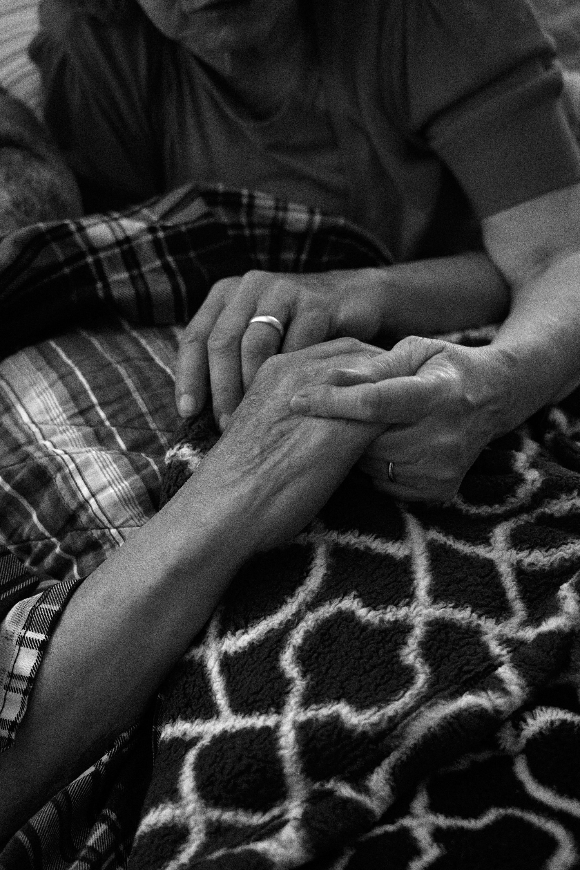 Elderly couple holding hands over a patterned blanket, showing signs of comfort and connection.