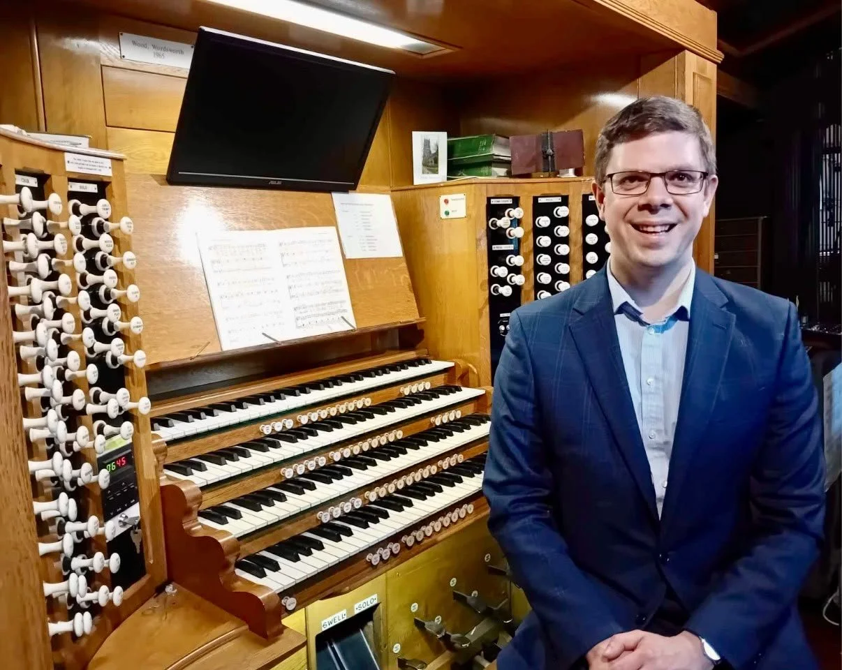 Alexander Woodrow, the hiking organist, is stood in front on the organ at Leeds Minster.