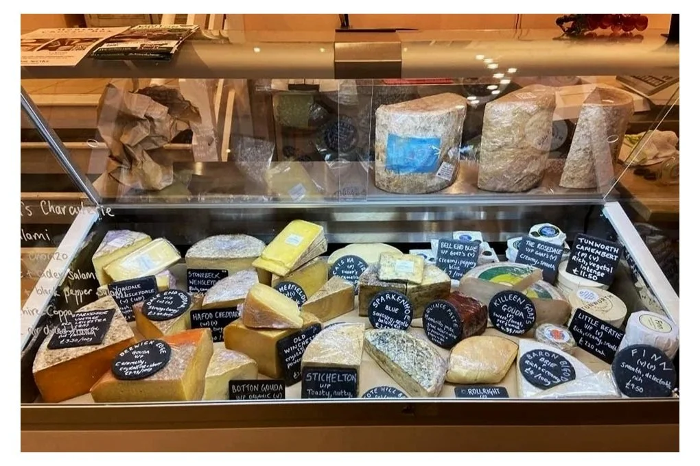 A range of cheeses in a fridge at a cheesemongers shop.