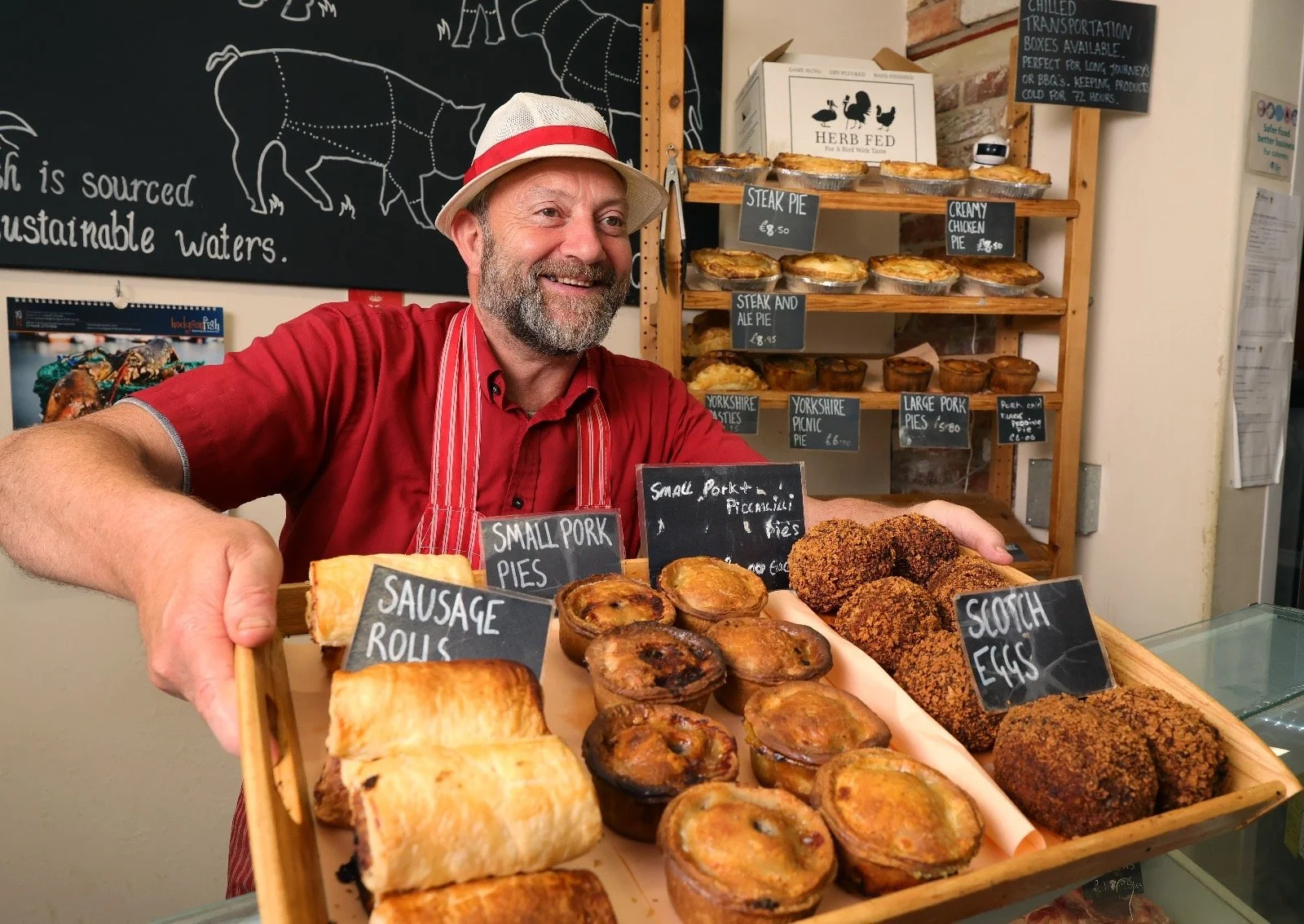 Owner of the business smiling holding a tray of pastries including sausage rolls, pork pies and scotch eggs