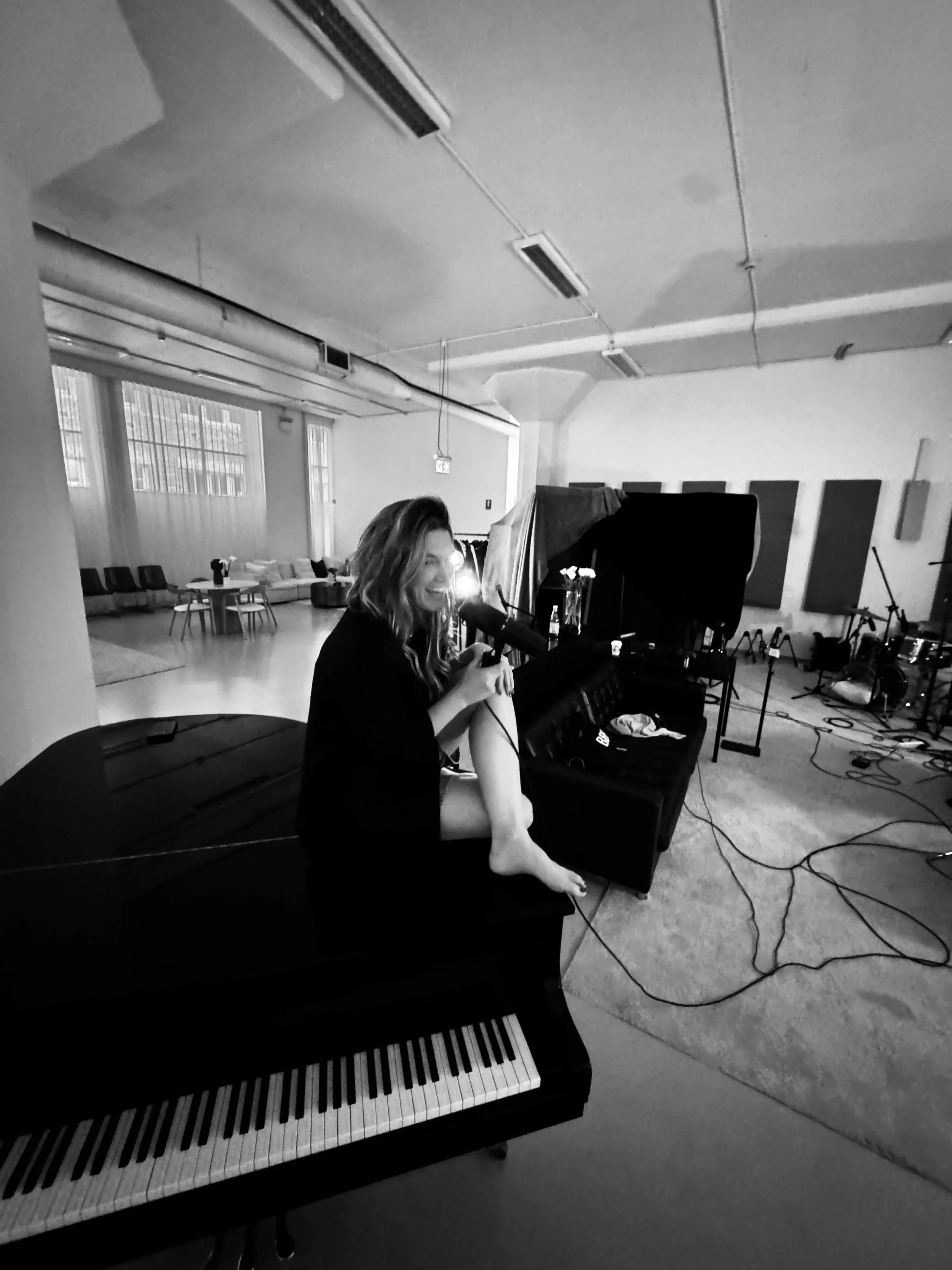 Delta Goodrem sitting on a grand piano holding a microphone in a photo taken by Jonas Myrin Behind The Scenes from the Eurovision Song Contest writing sessions of Eclipse with Jonas Myrin, Ferras Alqaisi and Michael Fatkin