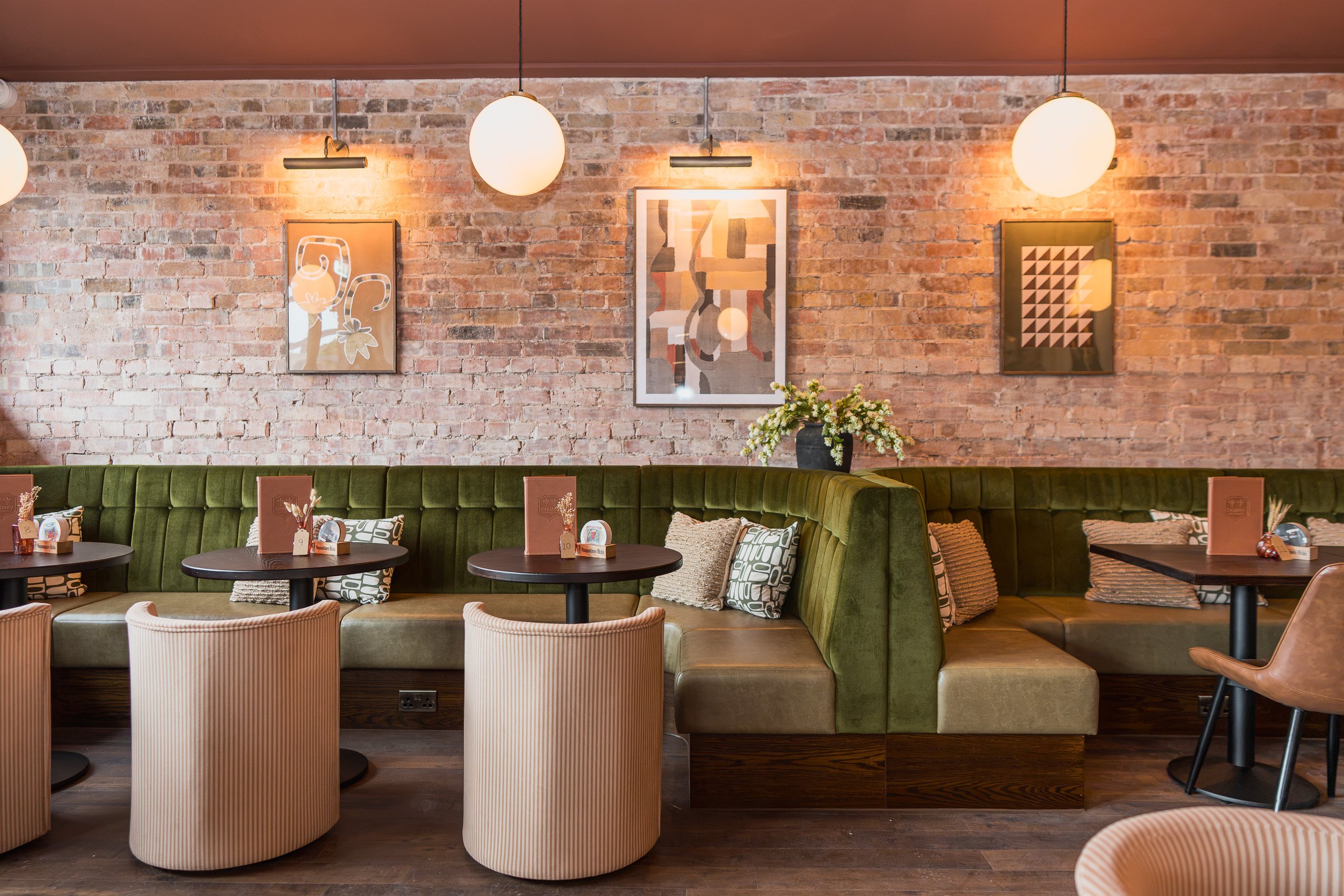 Green upholstered banquette, brick walls and pendant lighting at Hive Bar in Horsforth