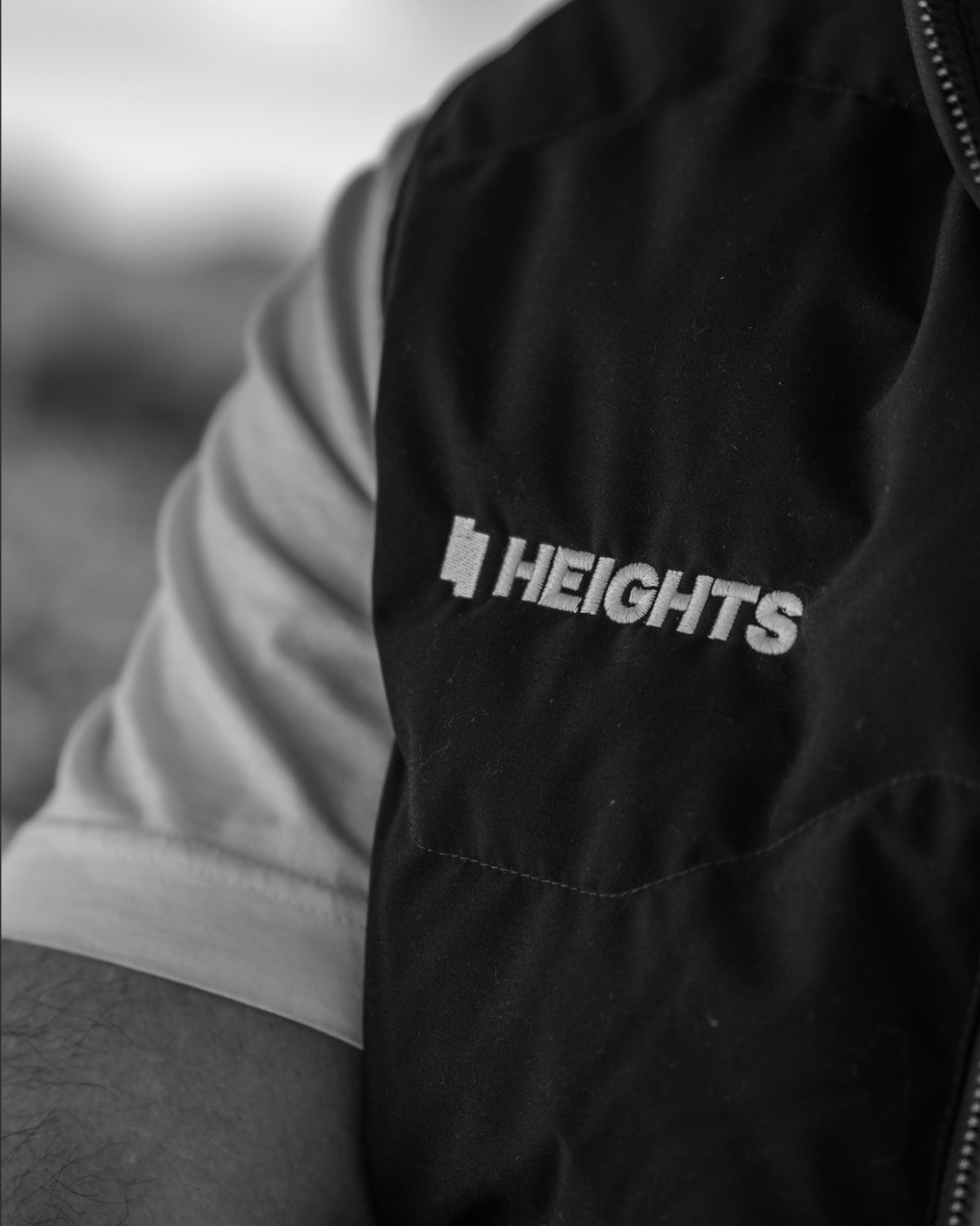 Close-up of a person wearing a black jacket with the word 'HEIGHTS' embroidered on it.