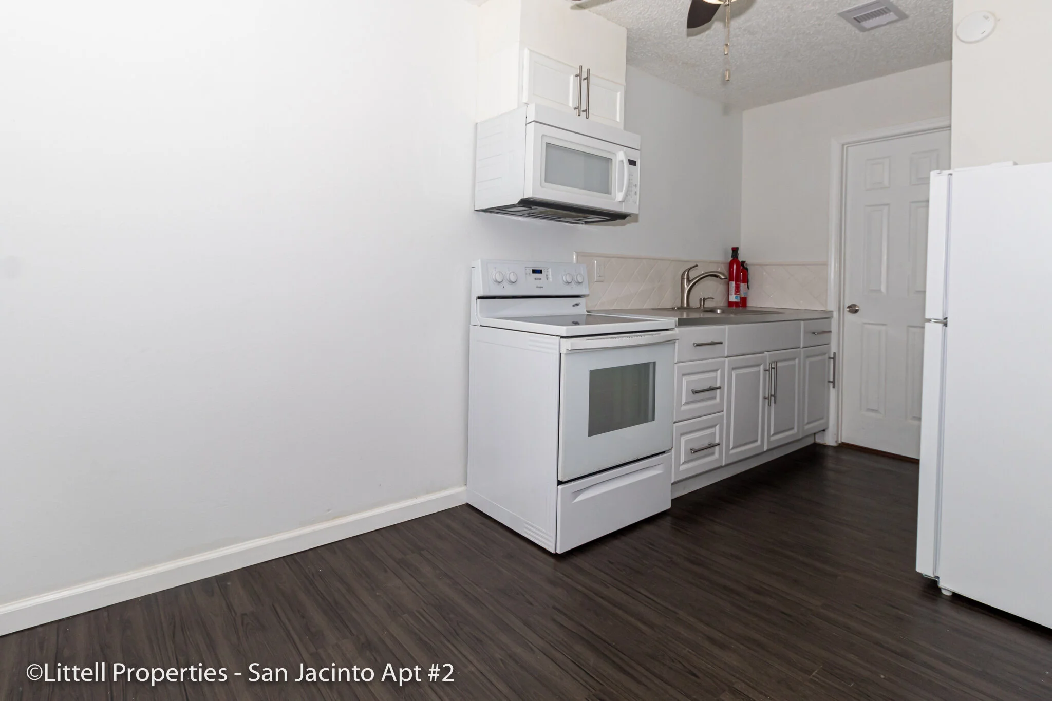 Kitchen: dark wood floor, stove/oven w/ microwave above. Countertop space around single sink. White cabinets below