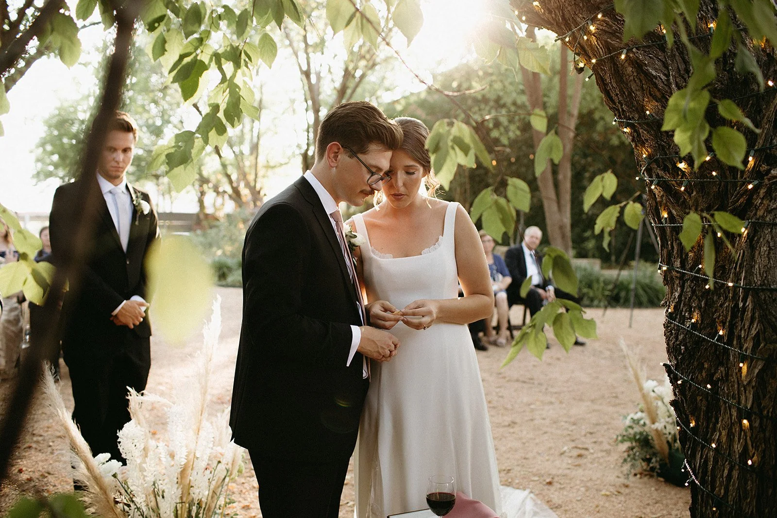 A bride and groom sharing a kiss during their wedding ceremony outdoors, surrounded by floral arrangements on a decorative rug.