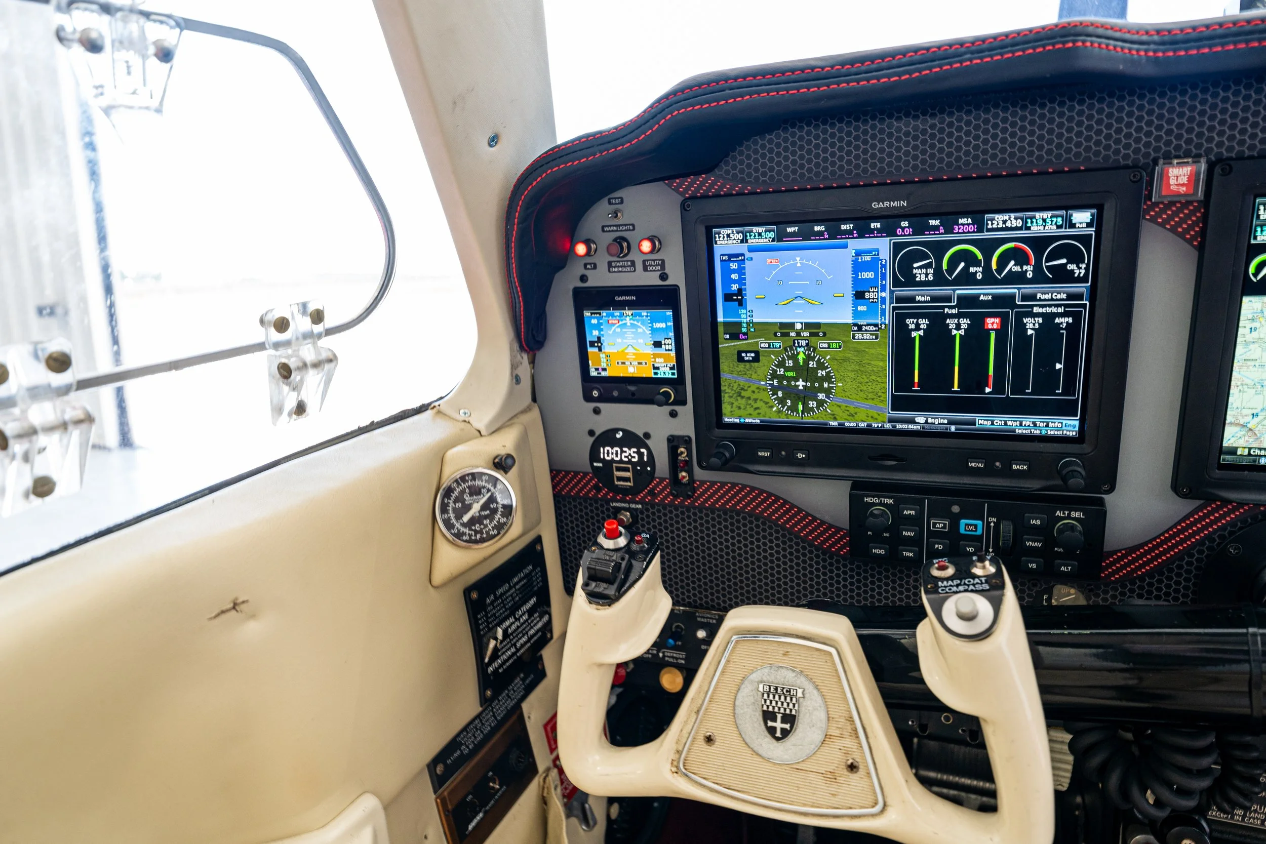 Inside the cockpit of a small aircraft, showing multiple digital flight instruments and controls, including GPS displays, engine gauges, and a beige interior.