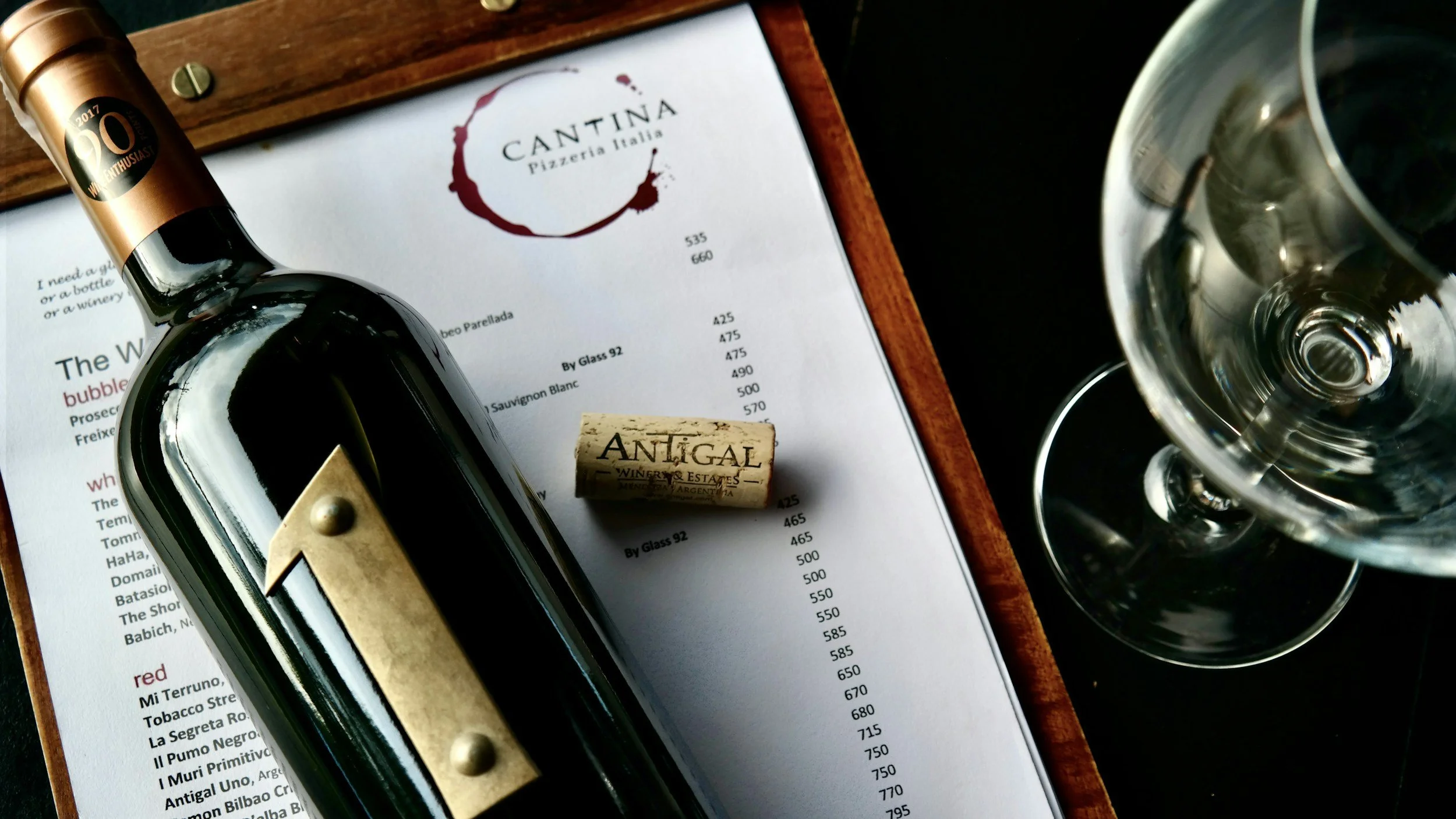 A wine bottle, a champagne cork, and a wine glass on a restaurant menu with a wooden frame.