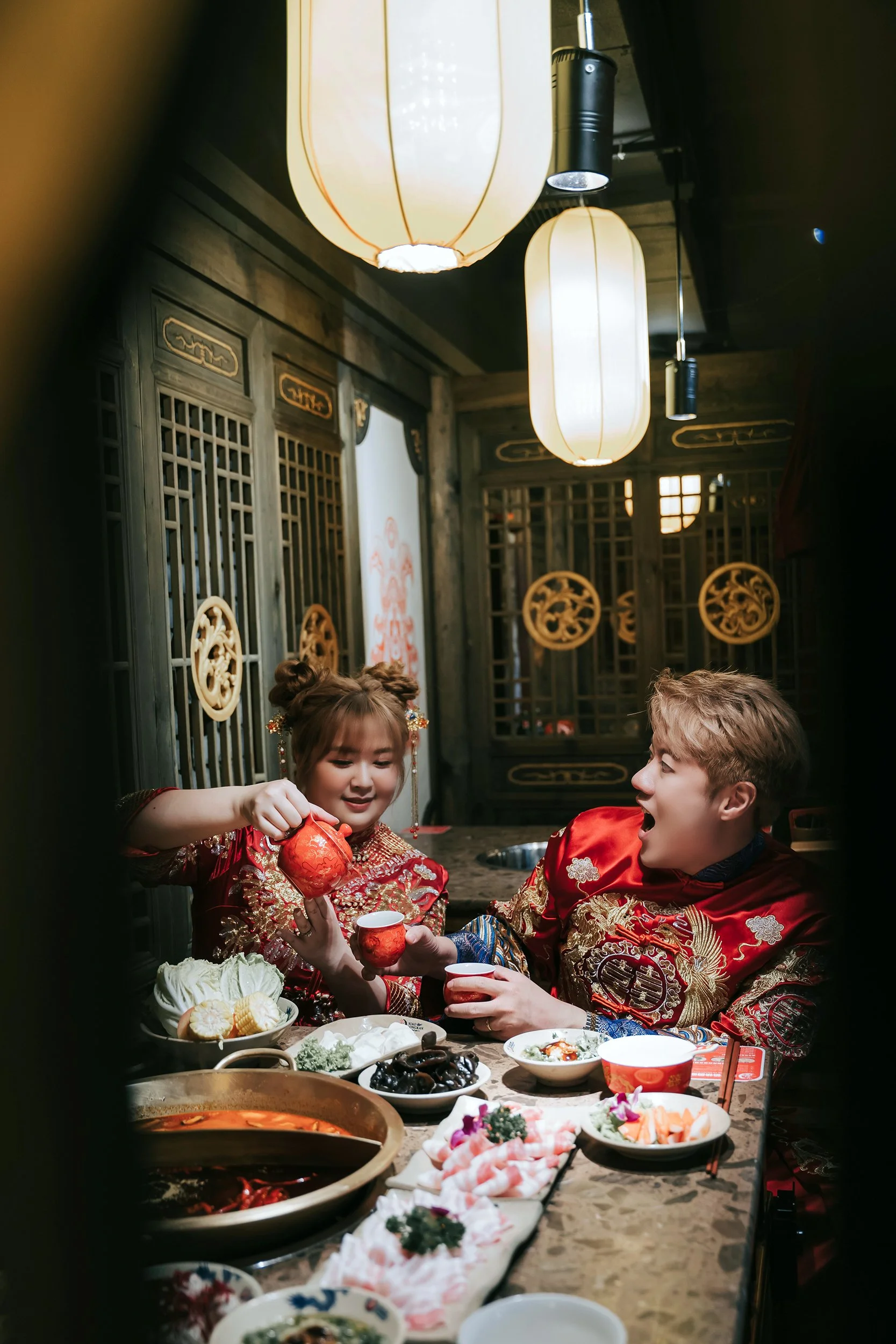 In the ornate ambiance of a traditional Chinese restaurant, Chris Ling Photography captures a delightful moment during a pre-wedding shoot. The couple, clad in resplendent red Chinese kua attire, seamlessly blend into the setting, echoing the rich cu