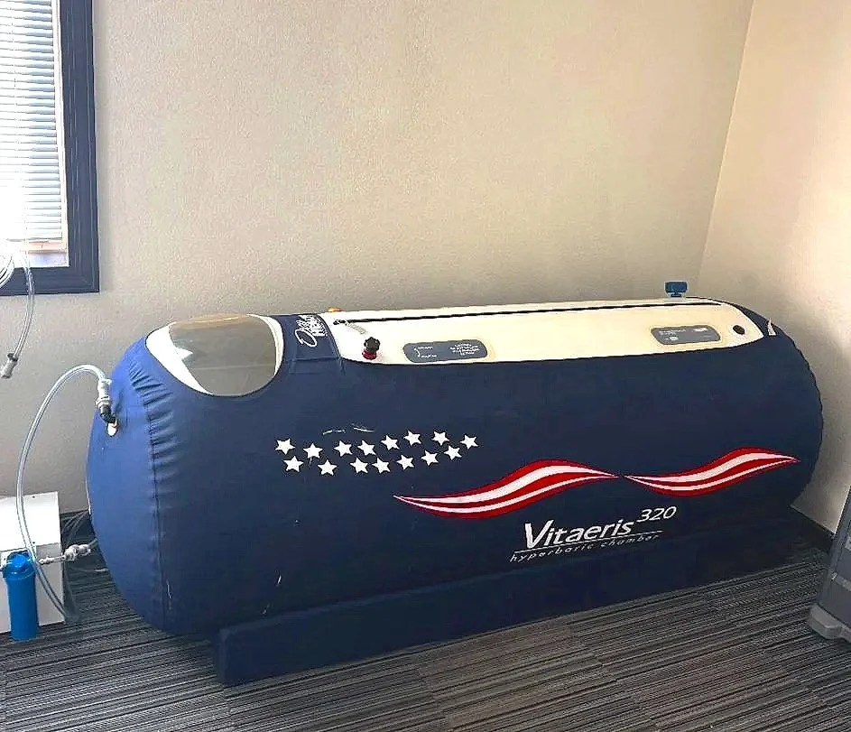 Hydrotherapy chamber with an American flag design, labeled Vitaeris 320, placed in a room with a window and a carpeted floor.