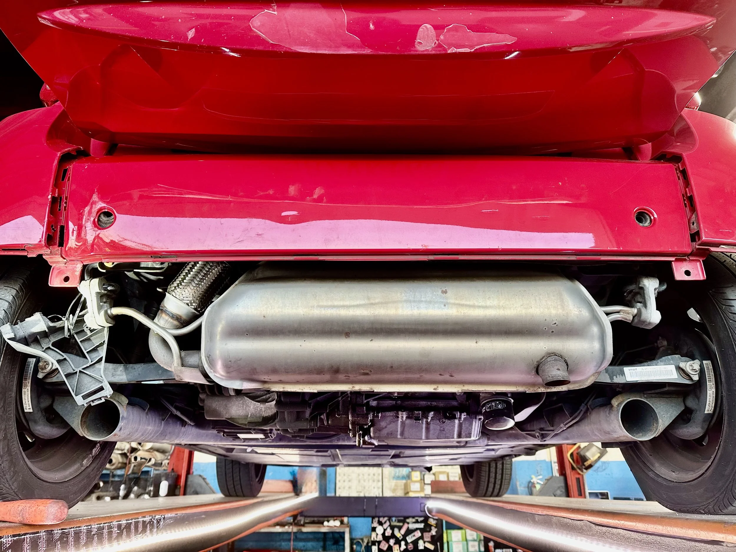Underneath a red sports car showing the exhaust system, muffler, and suspension components.