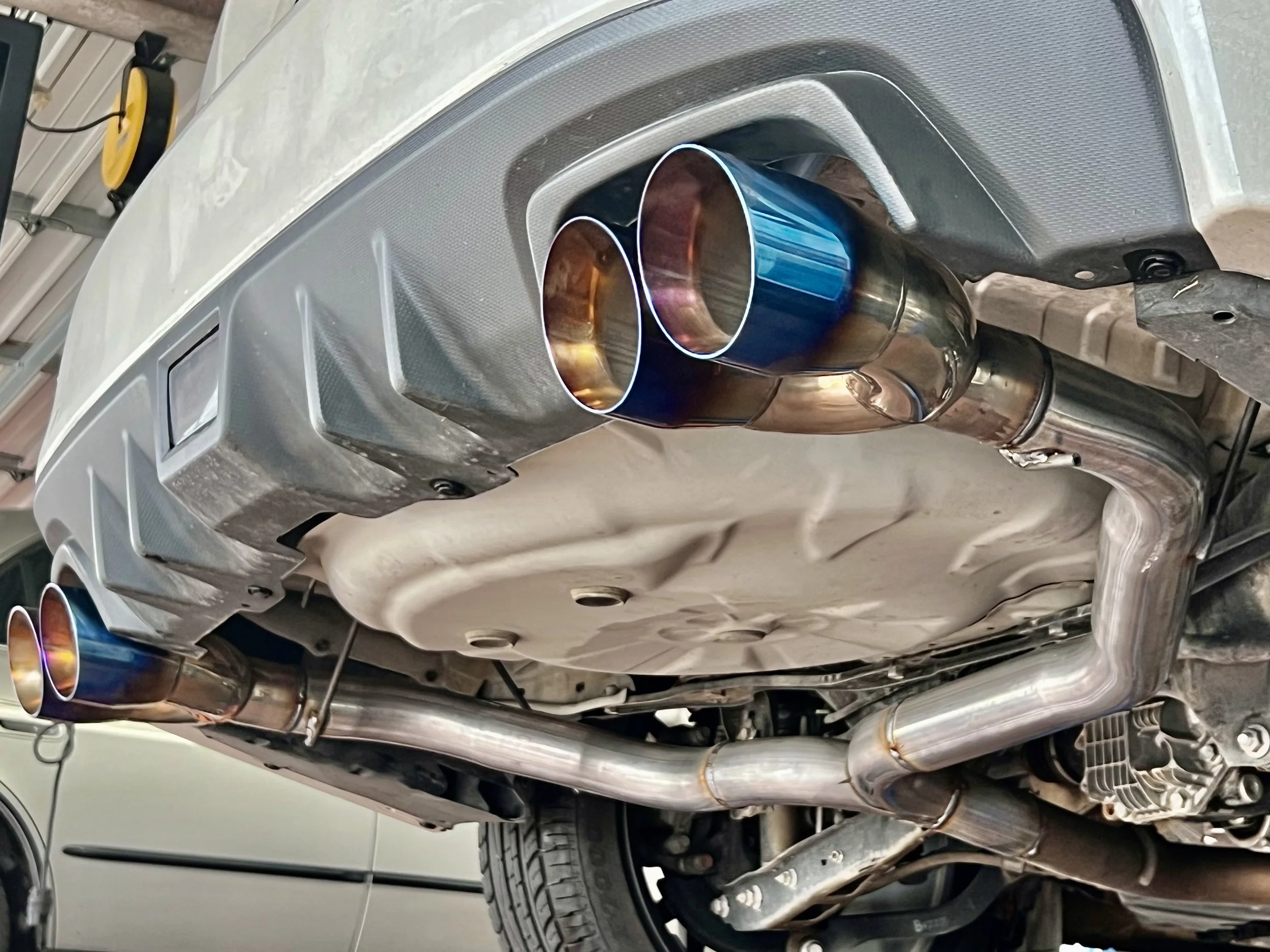 The underside of a car showing new aftermarket stainless steel exhaust pipes and mufflers.