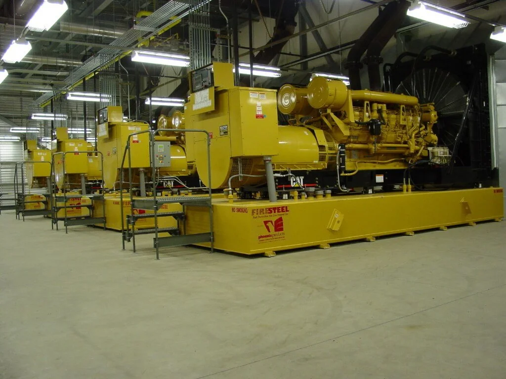 Large yellow industrial generators or engines in a manufacturing or utility facility.