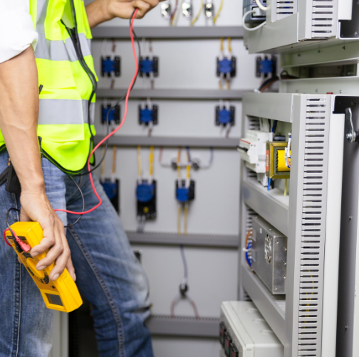 Technician working on electrical panel with multimeter in hand.