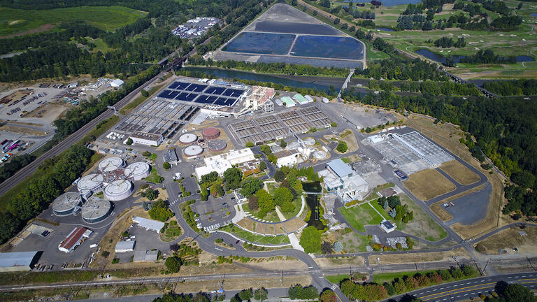 Aerial view of a water treatment plant with multiple tanks, processing units, and surrounding greenery.