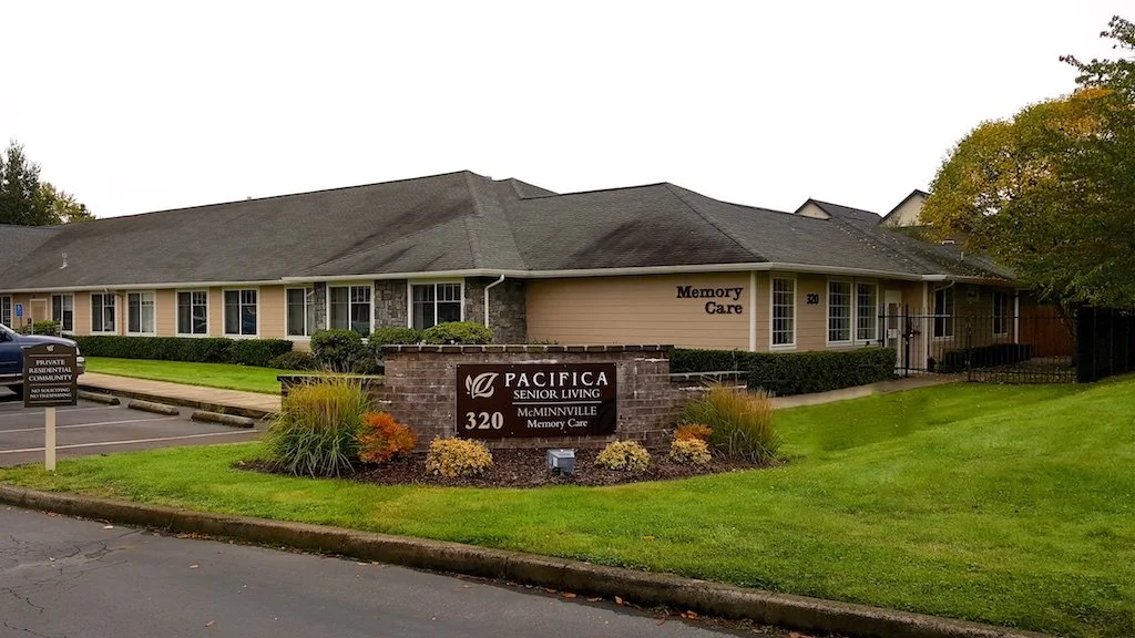 Exterior view of Pacifica Senior Living at 320 McMinnville Memory Care facility with well-maintained lawn, shrubs, and a parking lot.