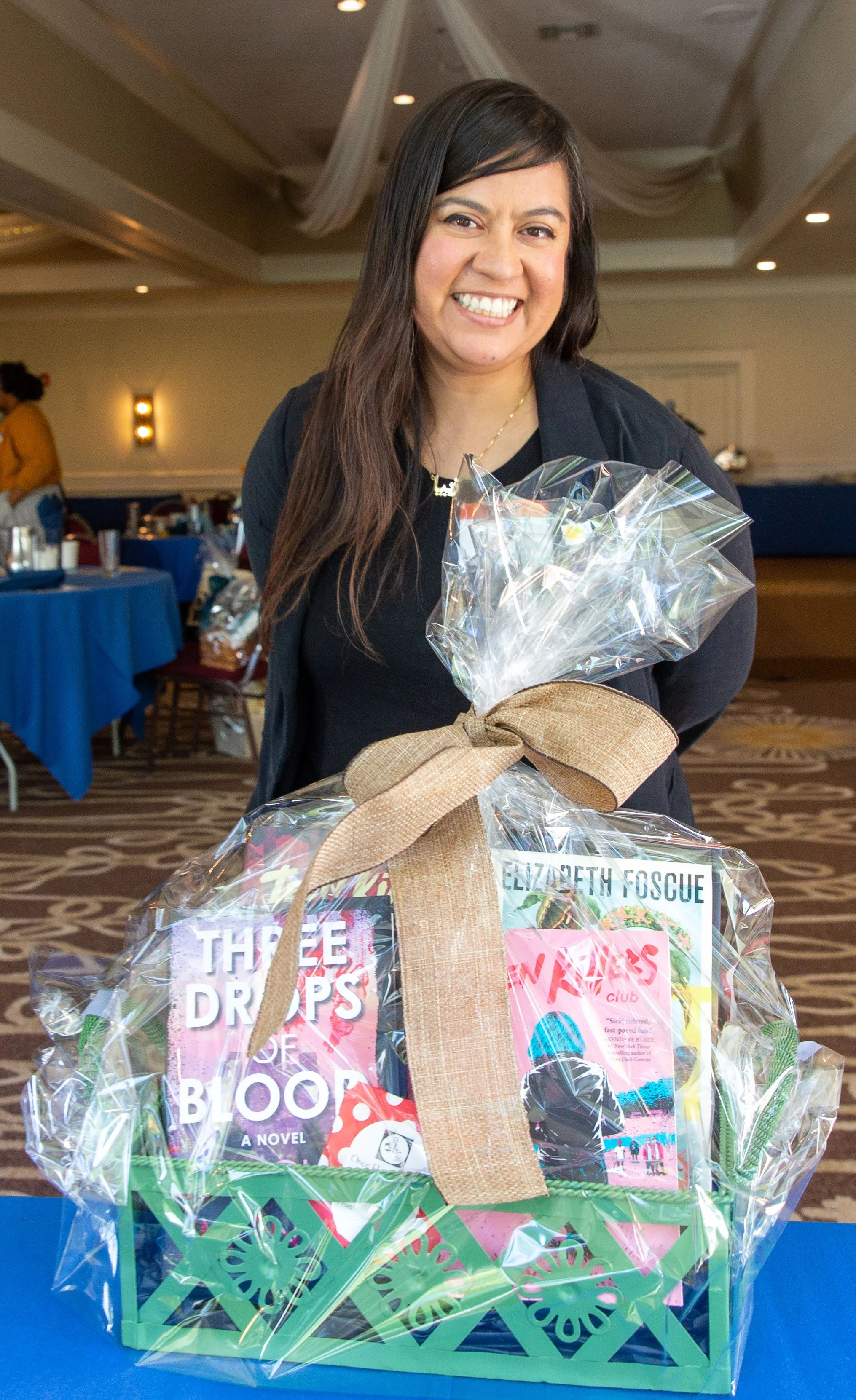 Silent auction winner Ziba Perez poses with the YA mystery-thriller basket, which includes Three Drops of Blood by Gretchen McNeil, Teen Killers Club by Lily Sparks, and Pest by Elizabeth Foscue. (Josh Steichmann)