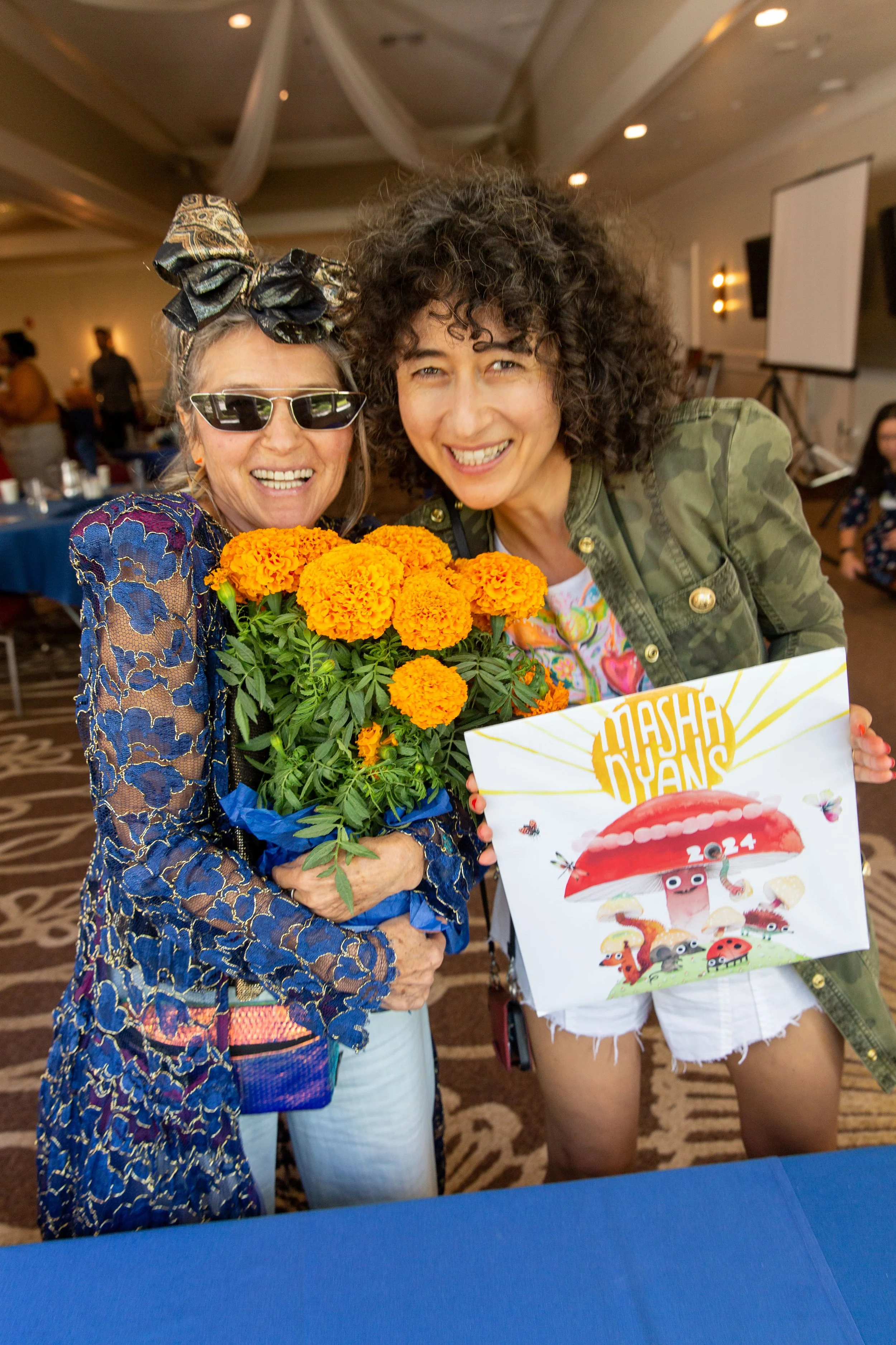 R to L: Award-winning author/illustrator Masha D'yans holds up her 2024 calendar beside her mother who is holding a marigold floral centerpiece. (Josh Steichmann)