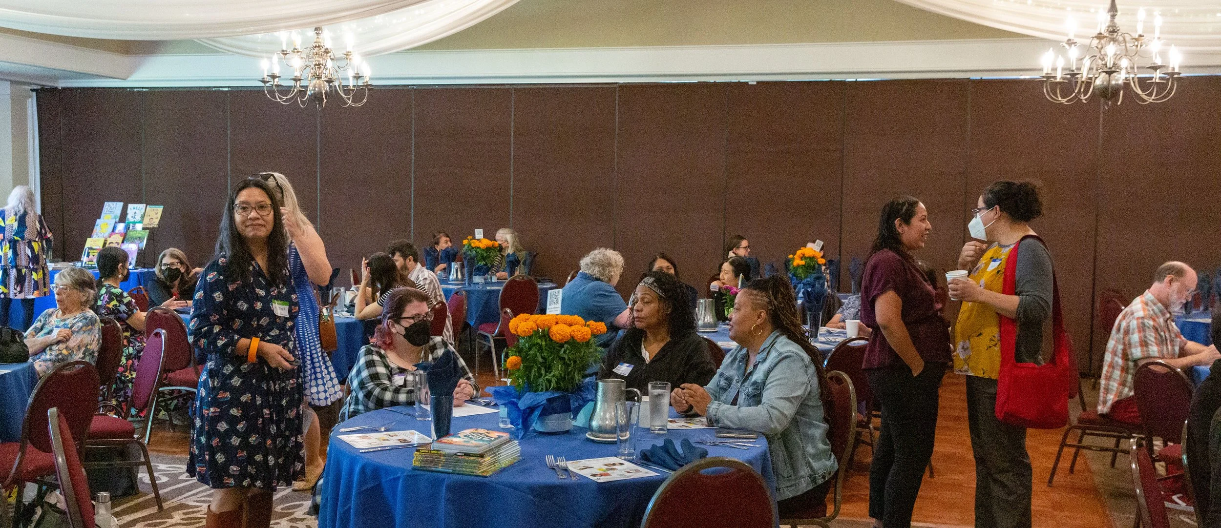 A candid photo shows a moment from the 2023 CLCSC Awards gathering in the Posada Room at Luminarias. On the left stands Awards Ceremony Chair Alethea Allarey. At the table in the center (L to R) are volunteer Kate Grieco, guest Marlene Narcisse, and