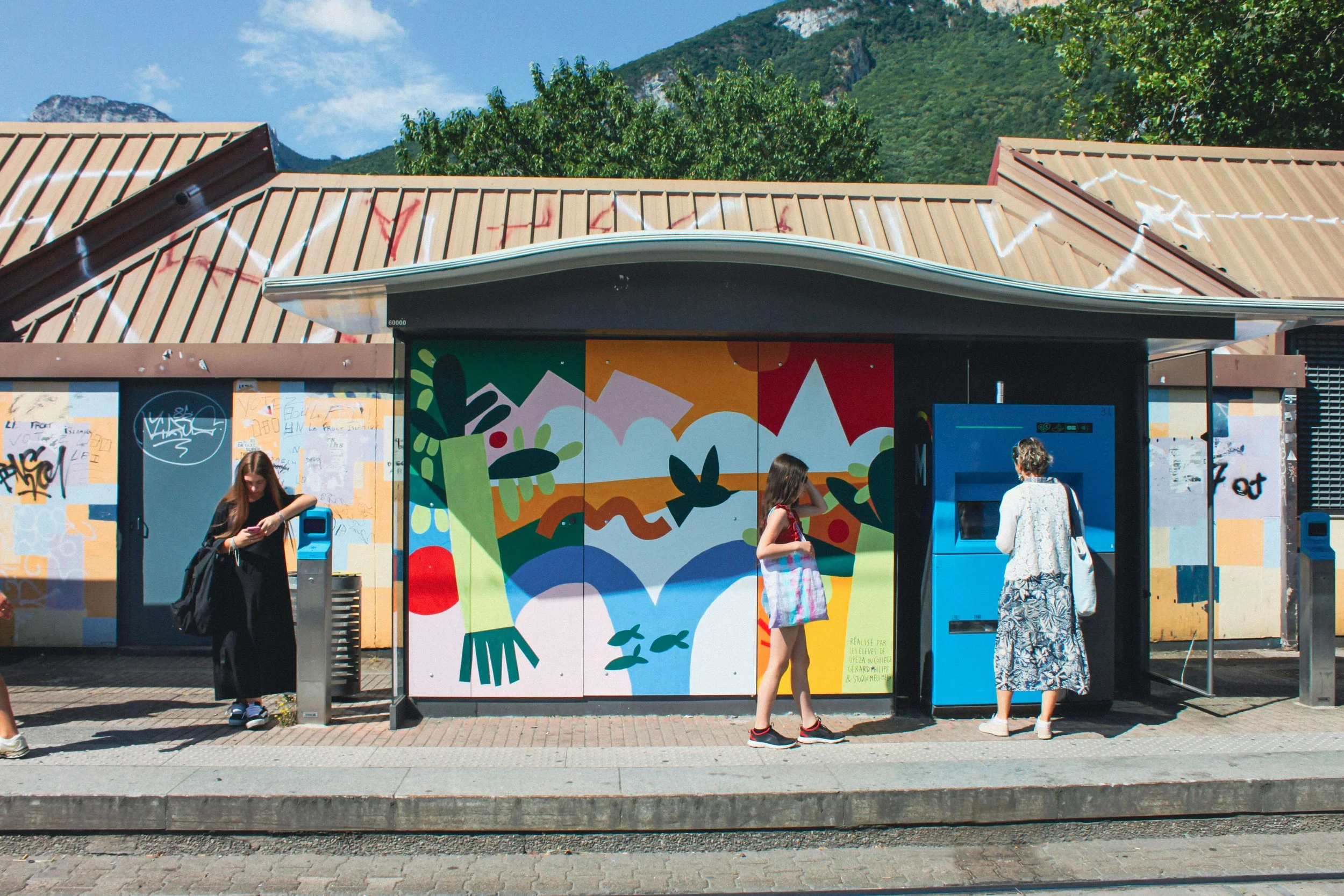 Des personnes attendent le tram à La Poya devant la fresque en peinture