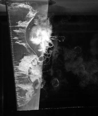 Figure 2: Cloud cavitation about a finite-span stainless steel hydrofoil exhibiting multiple shedding events along the span due to the re-entrant jet instability and span-wise compatibility of the cavitation. [3]