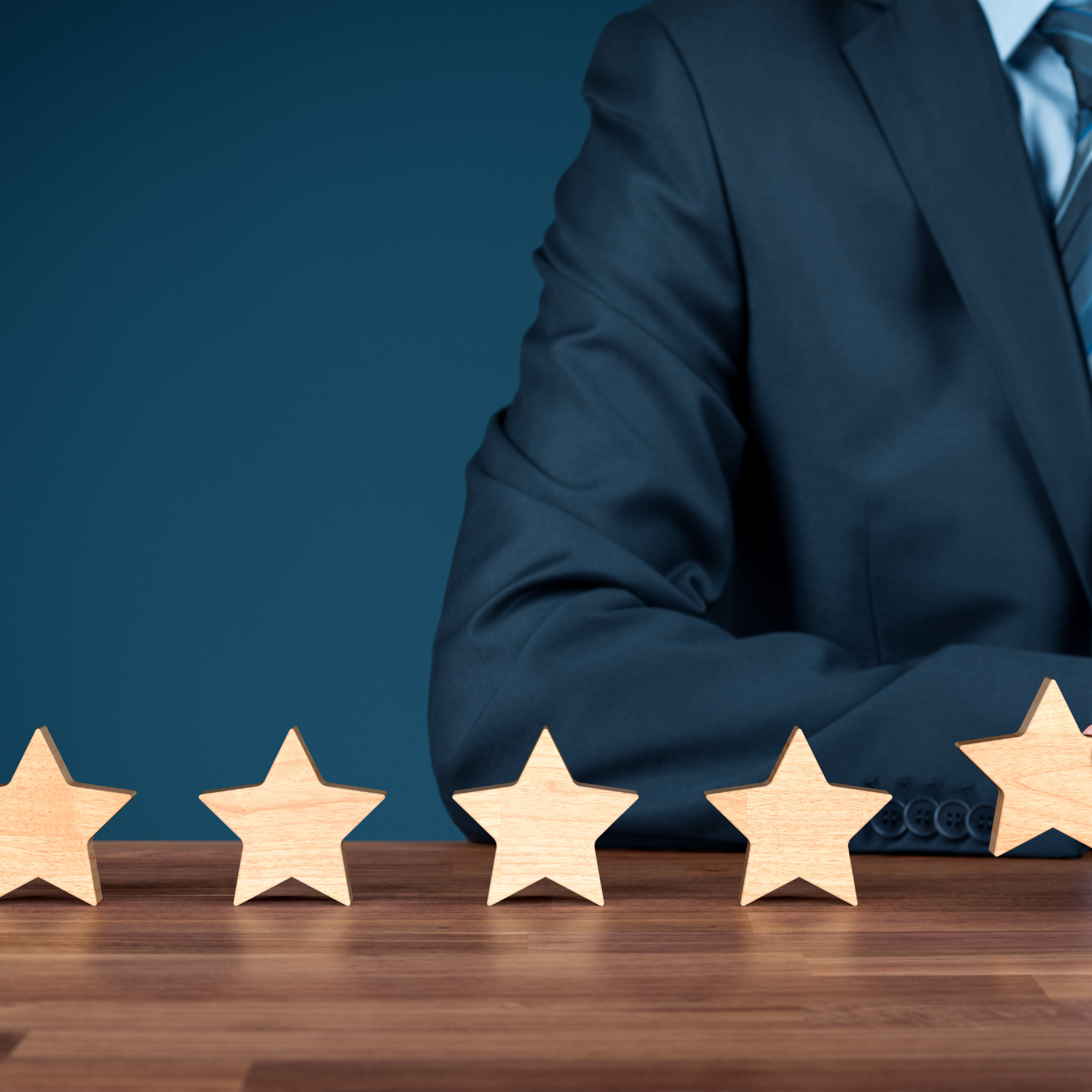 Five wooden stars on a table in front of a person in a suit, concept of quality or rating.