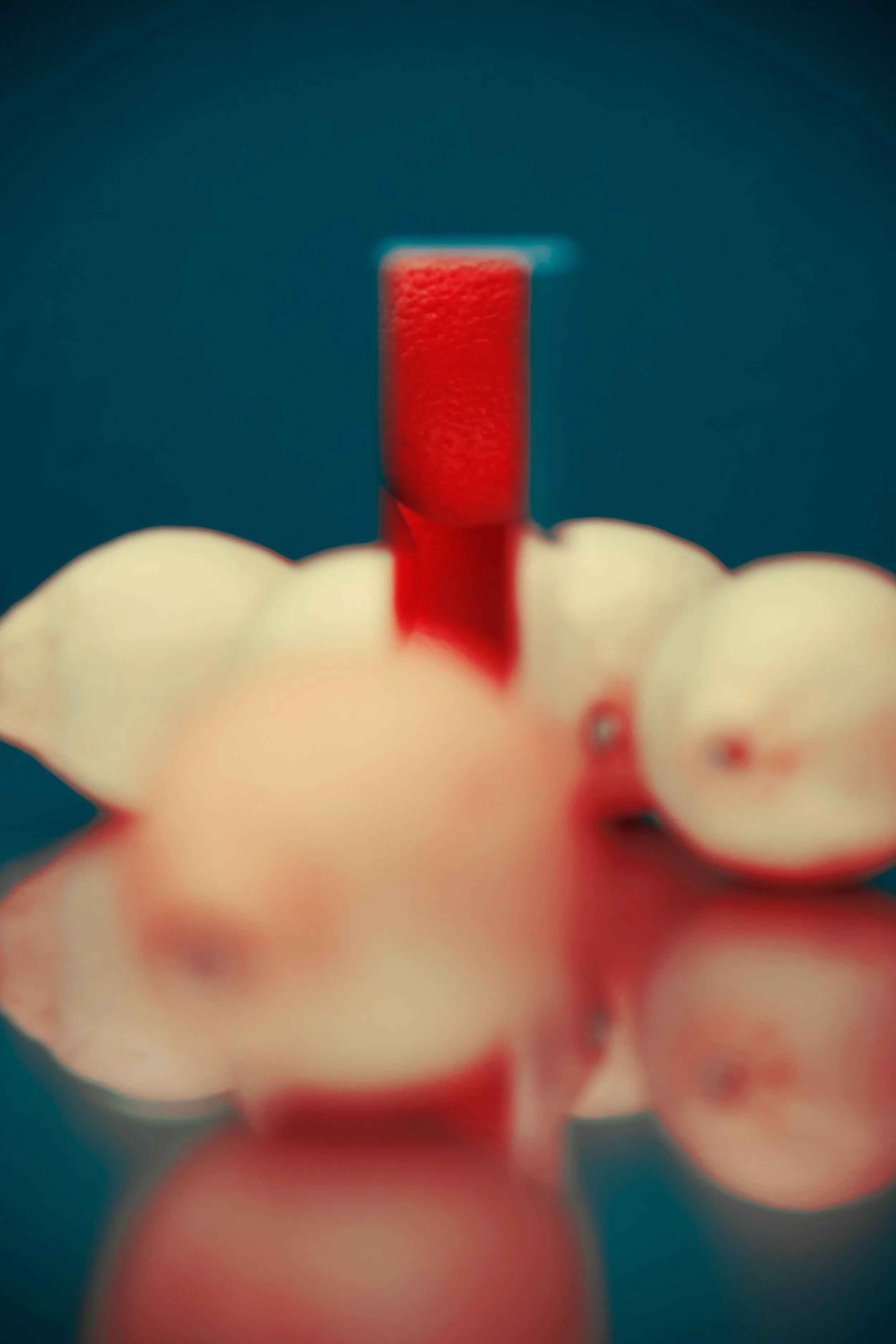 Close-up view of a red capsule pill with a bumpy surface, held above a collection of pink pills, against a dark background.