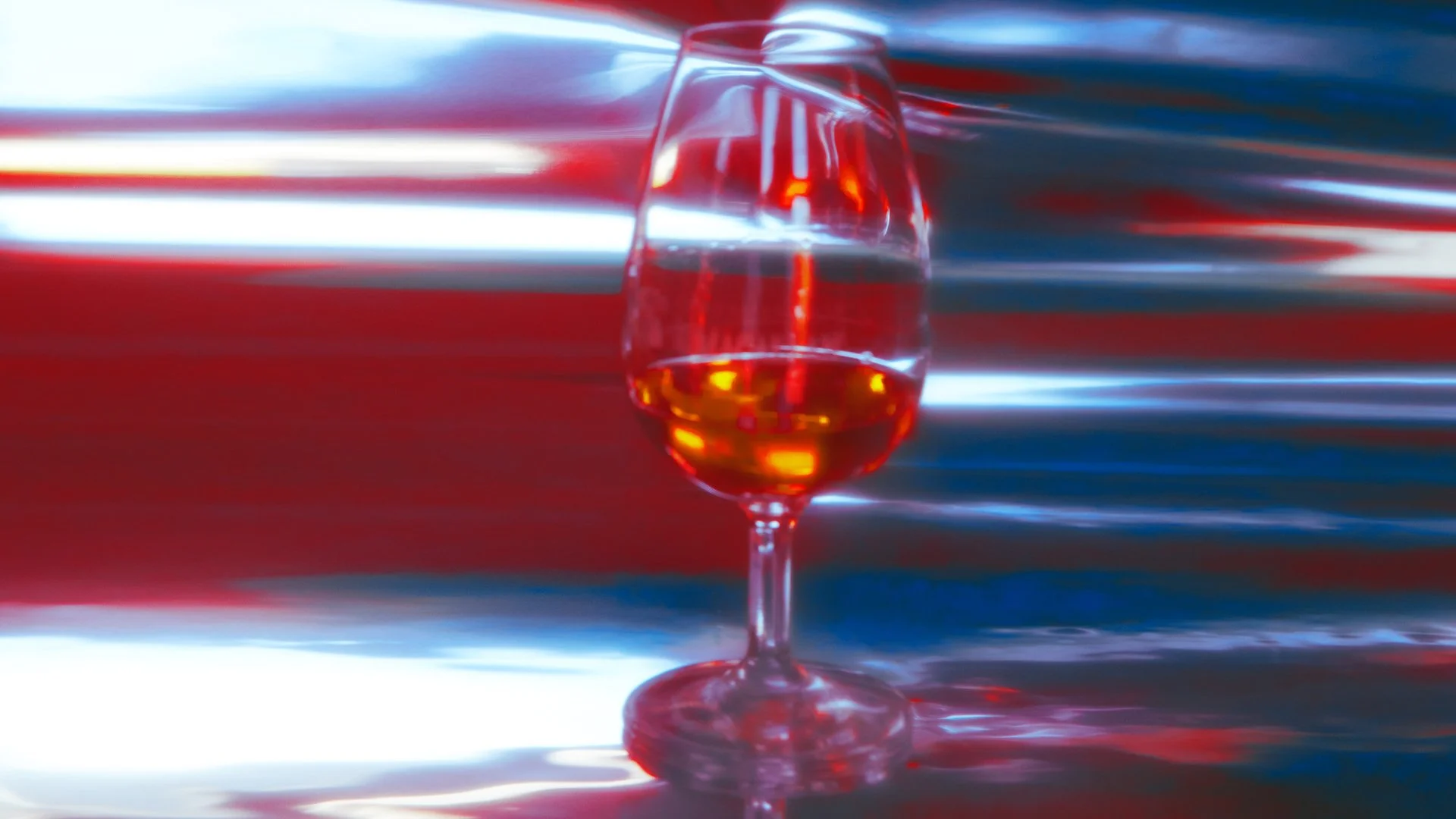 A glass of red wine on a reflective surface with colorful light streaks in the background.