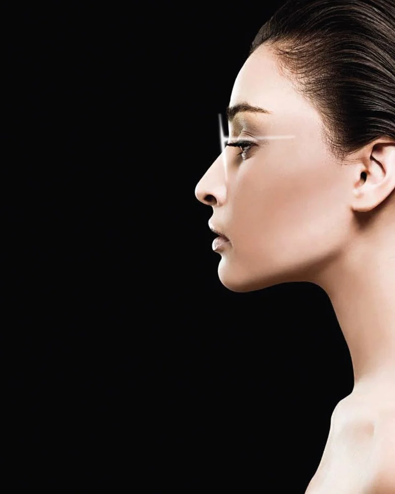 Side profile of a woman with sleek brown hair, closed eyes, and smooth skin against a black background.