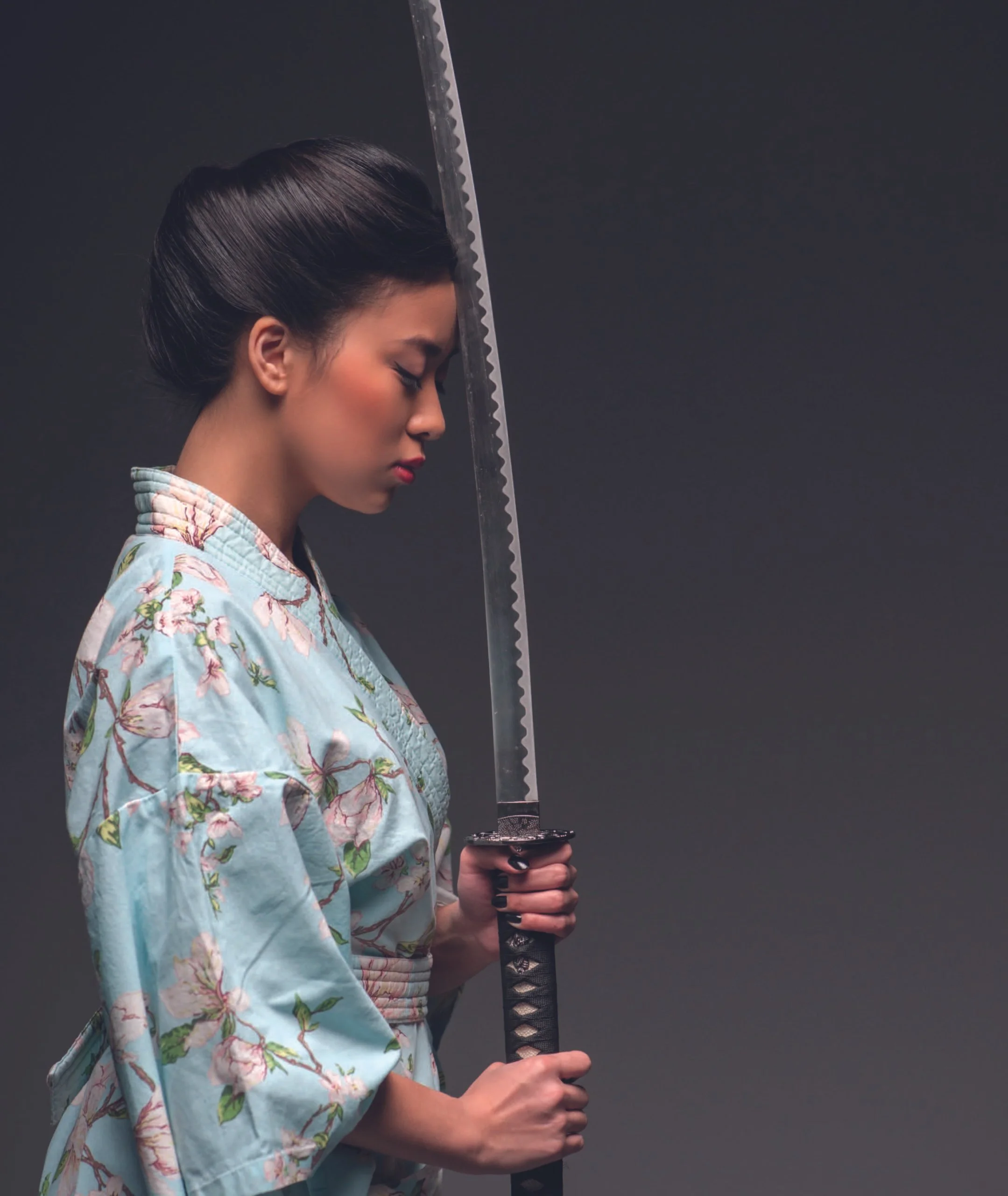 A woman dressed in a traditional Japanese kimono holding a katana sword with her eyes closed and head bowed.