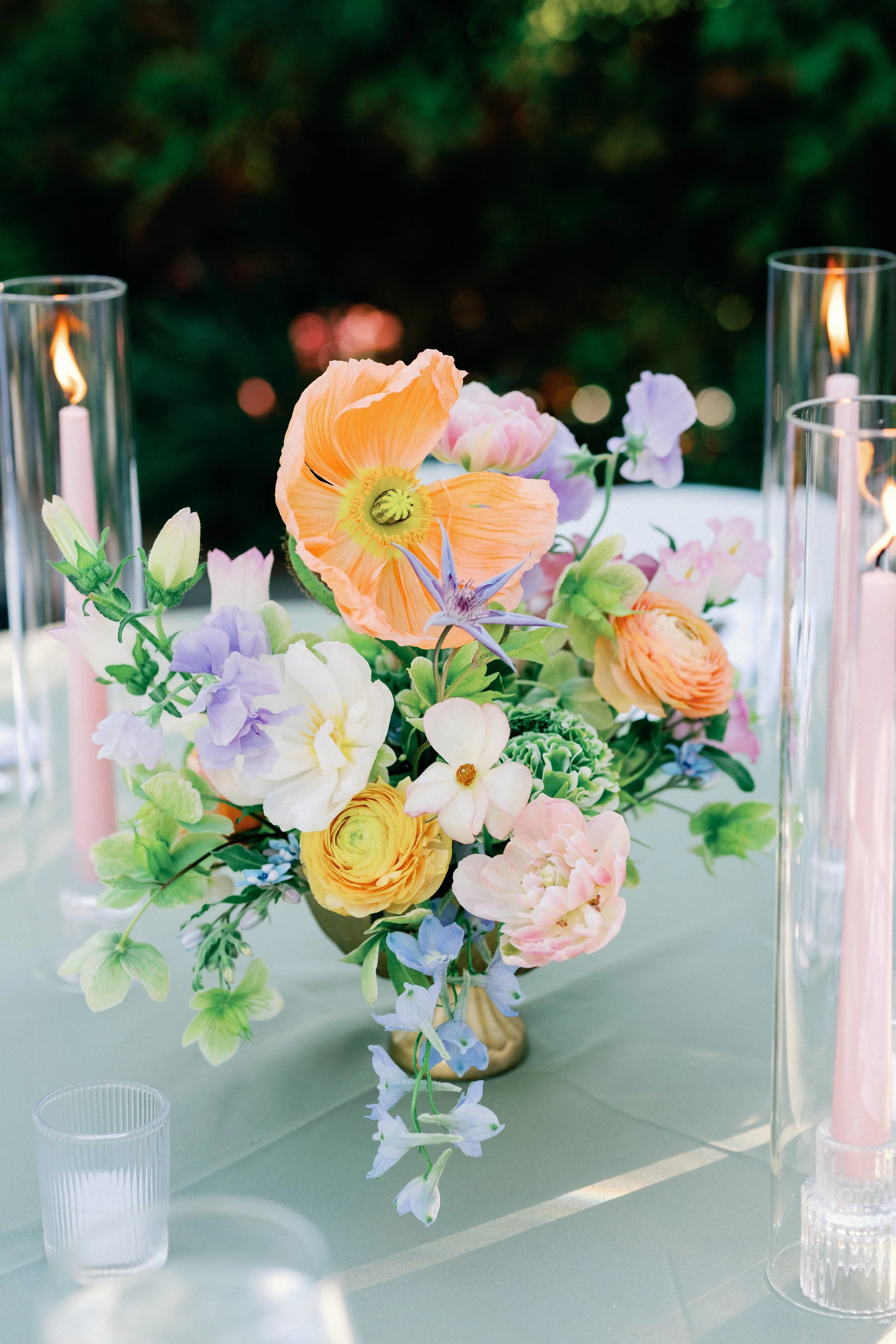 A stunning, whimsical floral centerpiece sits on a table between flickering candles at dusk.
