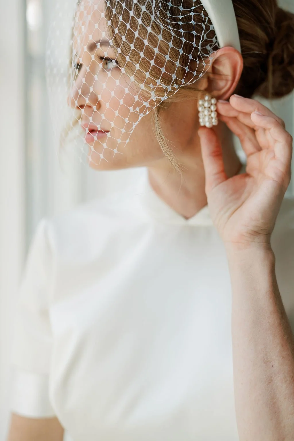 A Buckhead bride dressed in a stunning custom made Prada wedding gown looks out her window and touches her earring.