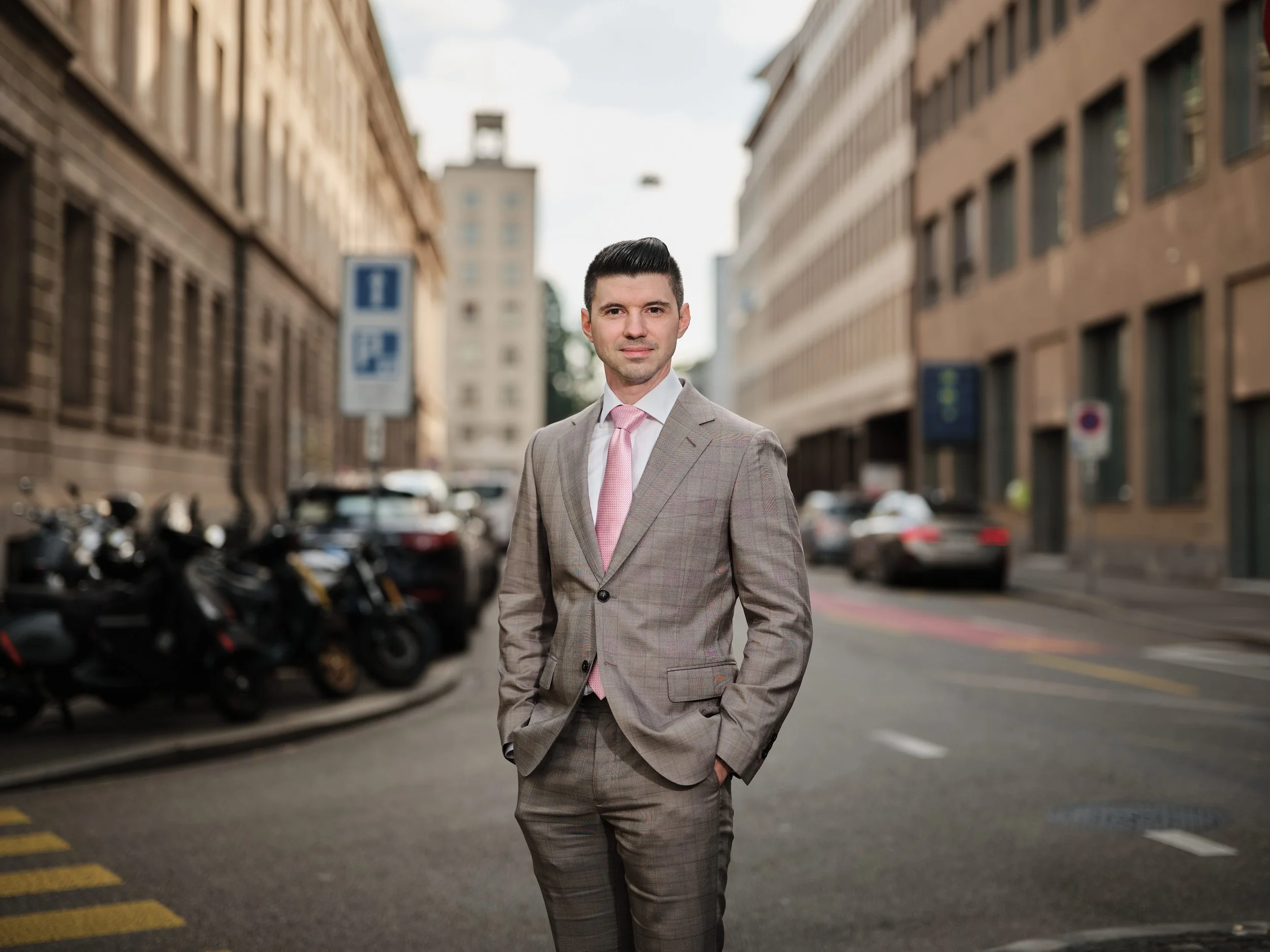 A man in a light brown business suit with a pink tie standing on a city street.