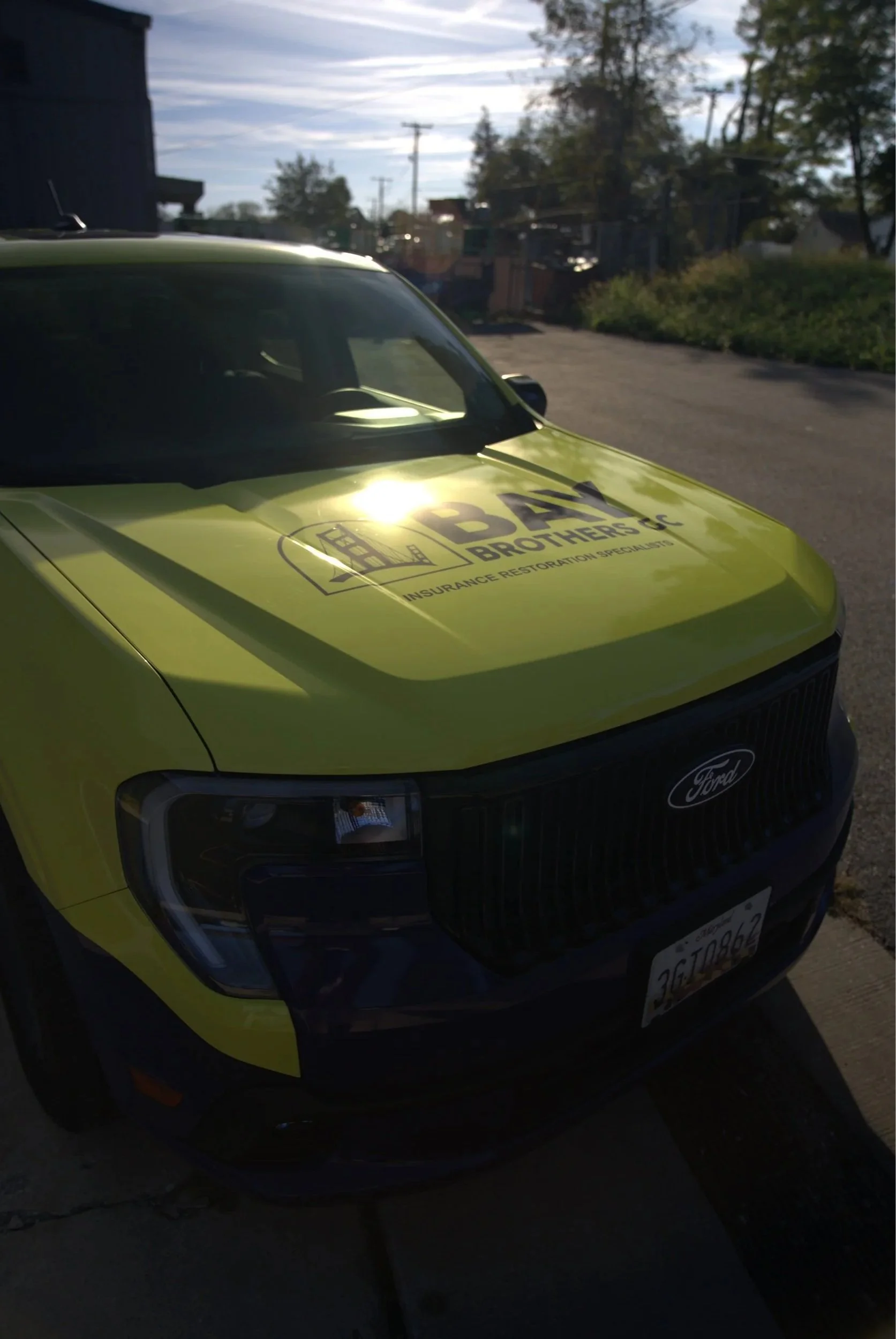A yellow Ford police vehicle with a logo and words 'BEAM BROTHERS' and 'Insurance Restoration Specialists' on the hood, parked outdoors with trees and utility poles in the background.