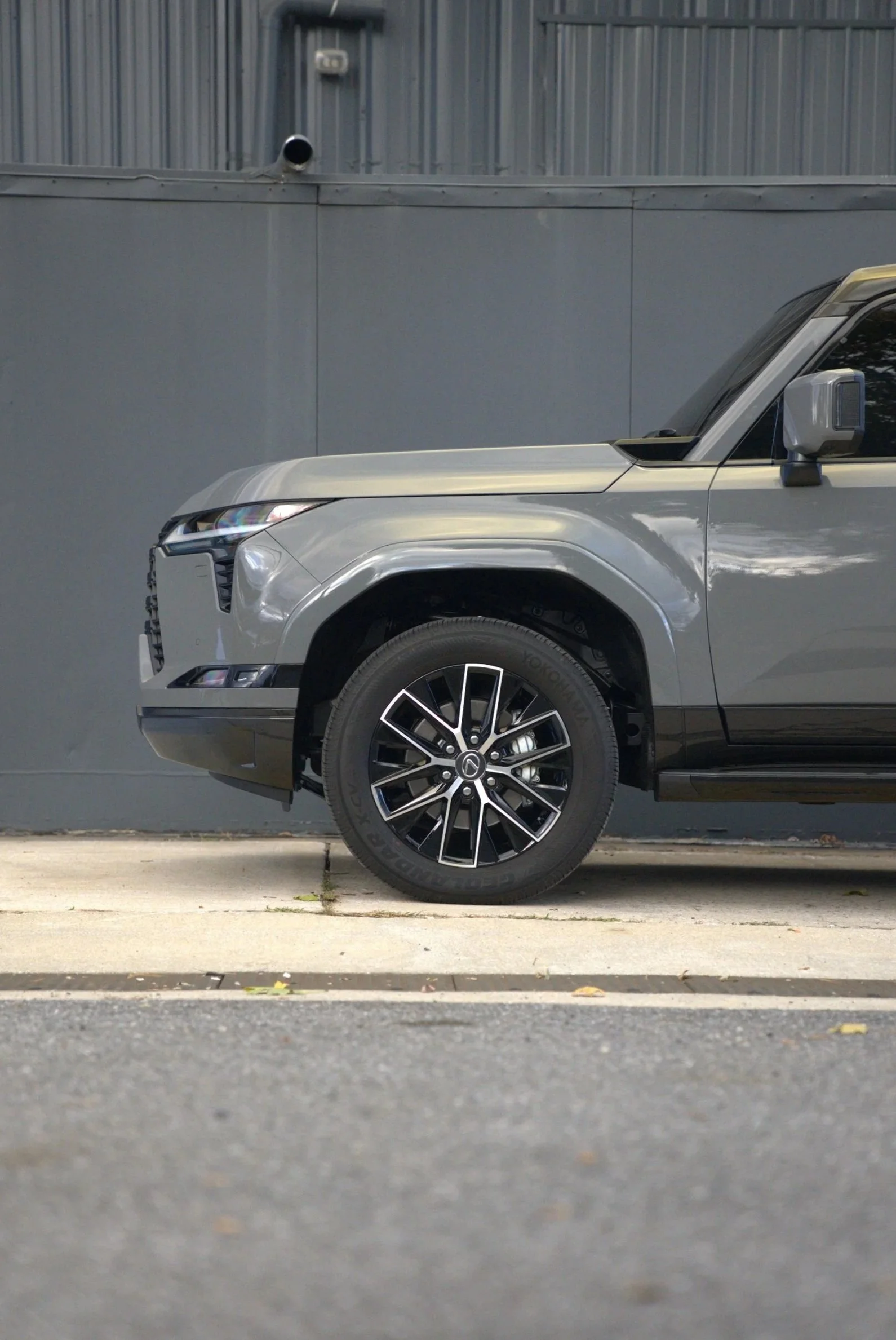 Side view of a modern silver SUV parked on a curb in front of a gray wall.