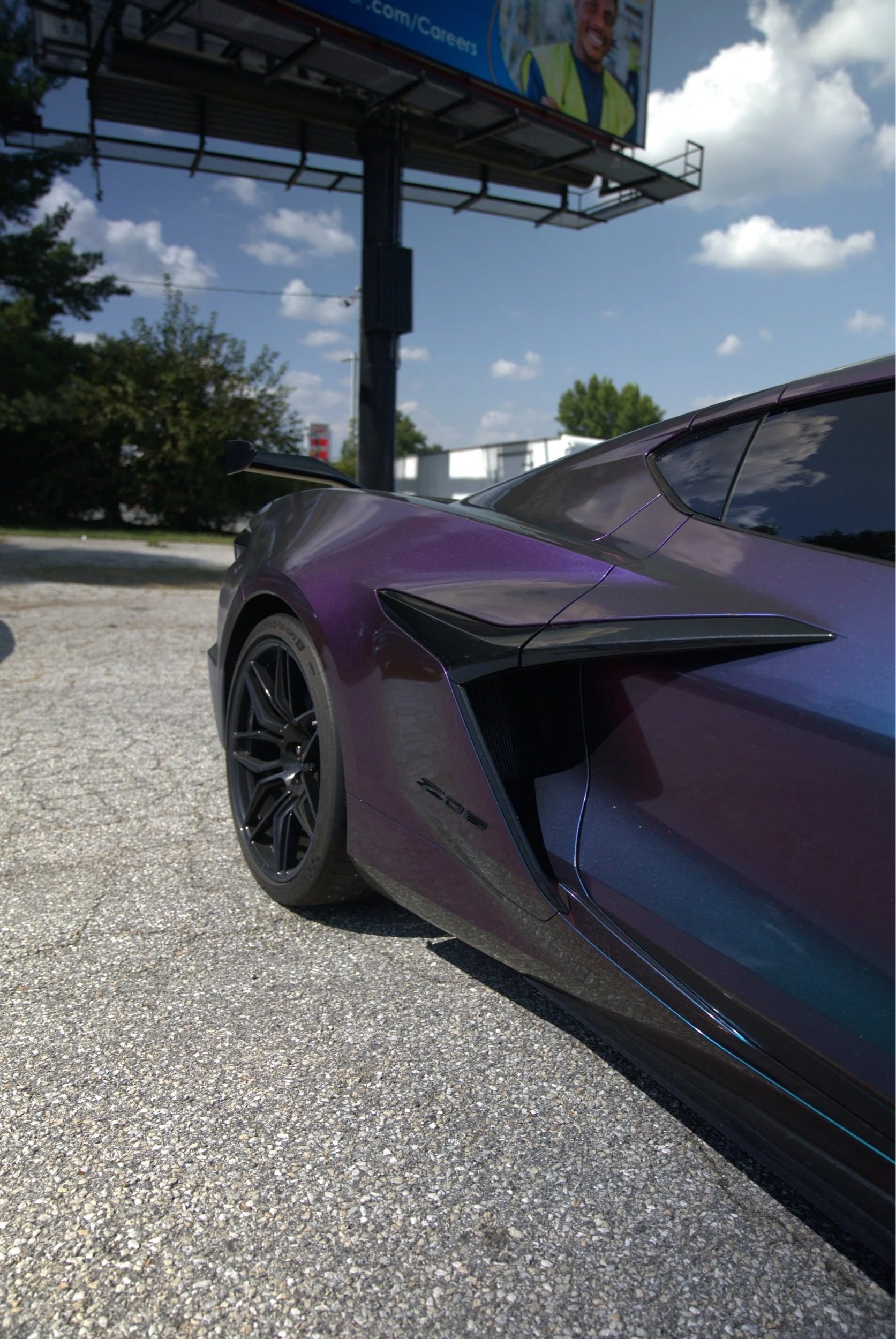Close-up of a purple sports car parked on a gravel lot, showing the front and side with a focus on the wheel, air vent, and sleek design.