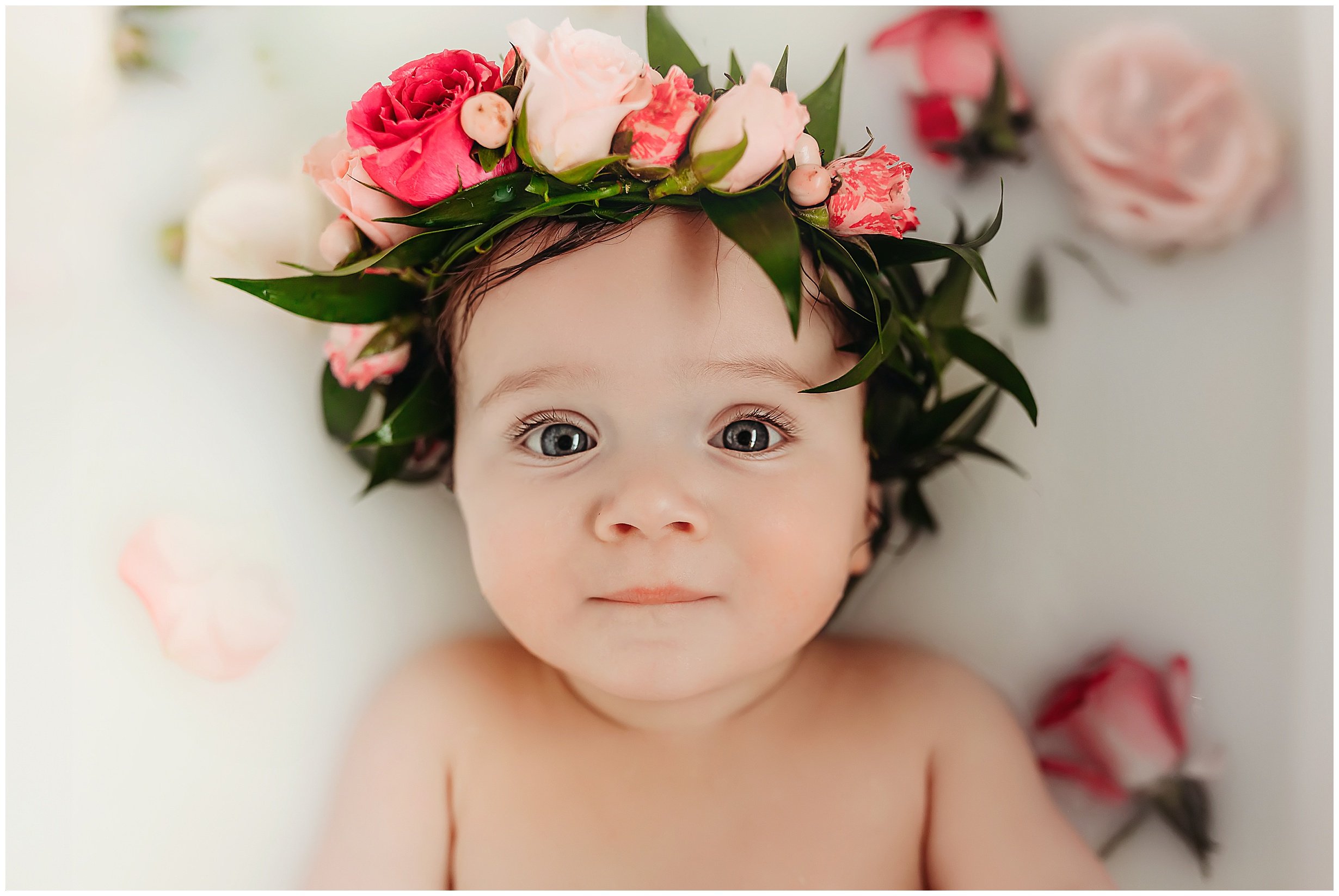 Baby girl enjoying a milk bath with a crown of flowers on her head