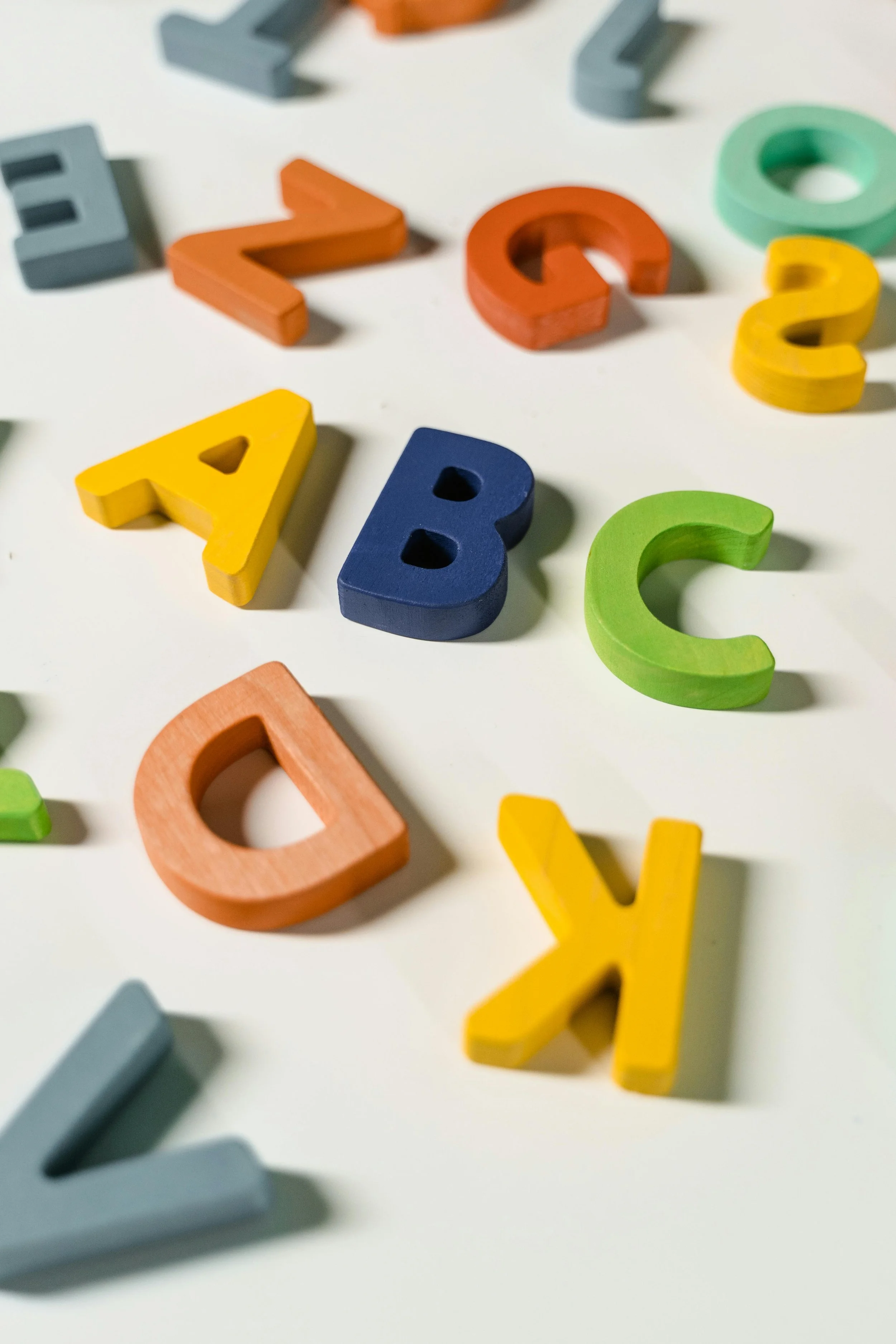 Colorful wooden letters scattered on a white surface, including A, B, C, D, and other characters in various colors.