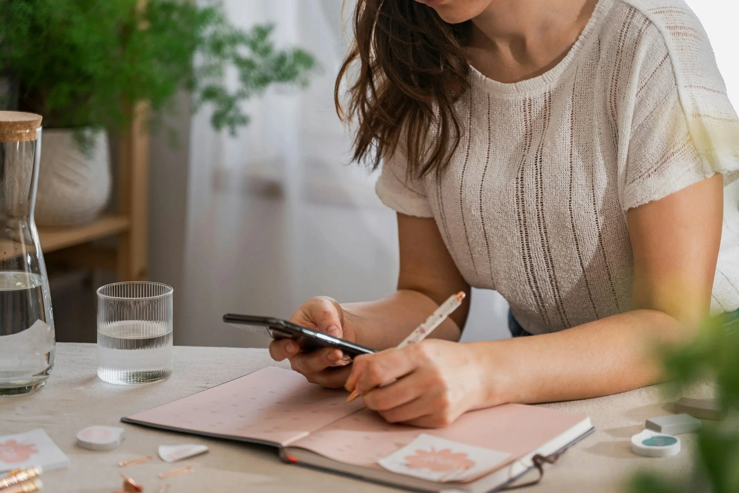 Woman looking at her phone and writing in her planner, showing how anxious women get stuck in overthinking. Holistic therapy for anxiety in Charlotte, NC can help to reduce this anxiety.