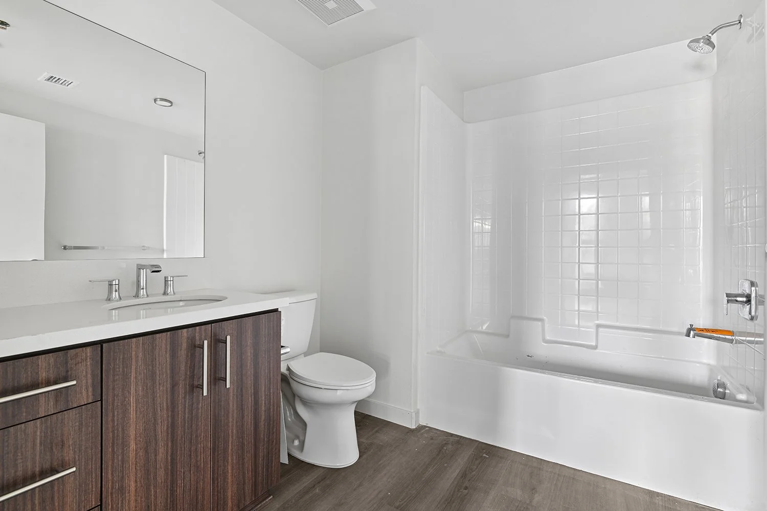 Luxurious bathroom in Rendezvous Phase II bathroom with wood-style plank flooring, large vanity with quartz countertops, modern dark walnut cabinets, and a shower/tub. 
