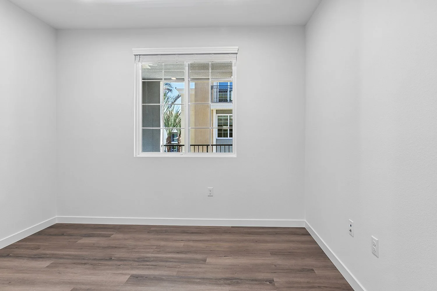 Bedroom in Rendezvous Phase II apartment home with wood-style plank flooring and window looking out to private patio. 