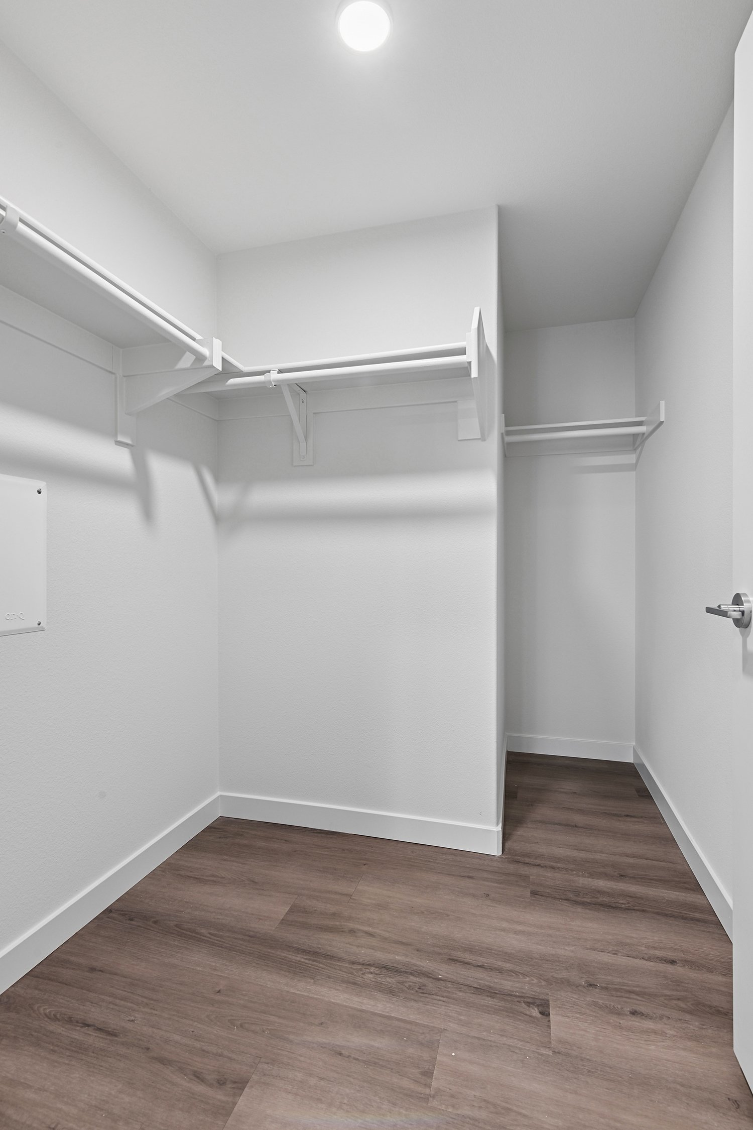 Walk-in closet with wood-style plank flooring and built in shelving with hanging rods. 