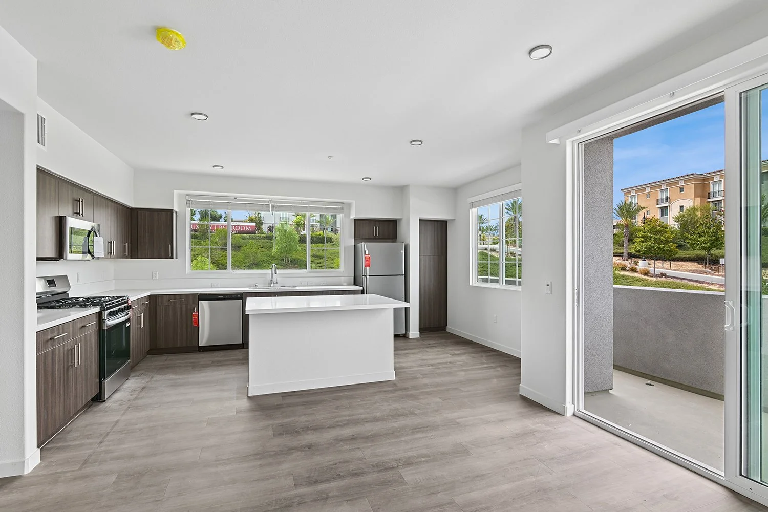 Spacious open concept living area leading to kitchen in Rendezvous Phase II apartment home. Wood-style plank flooring, modern dark walnut cabinetry, stainless steel appliances, quartz countertops, island, and a lot of windows allowing for gorgeous na