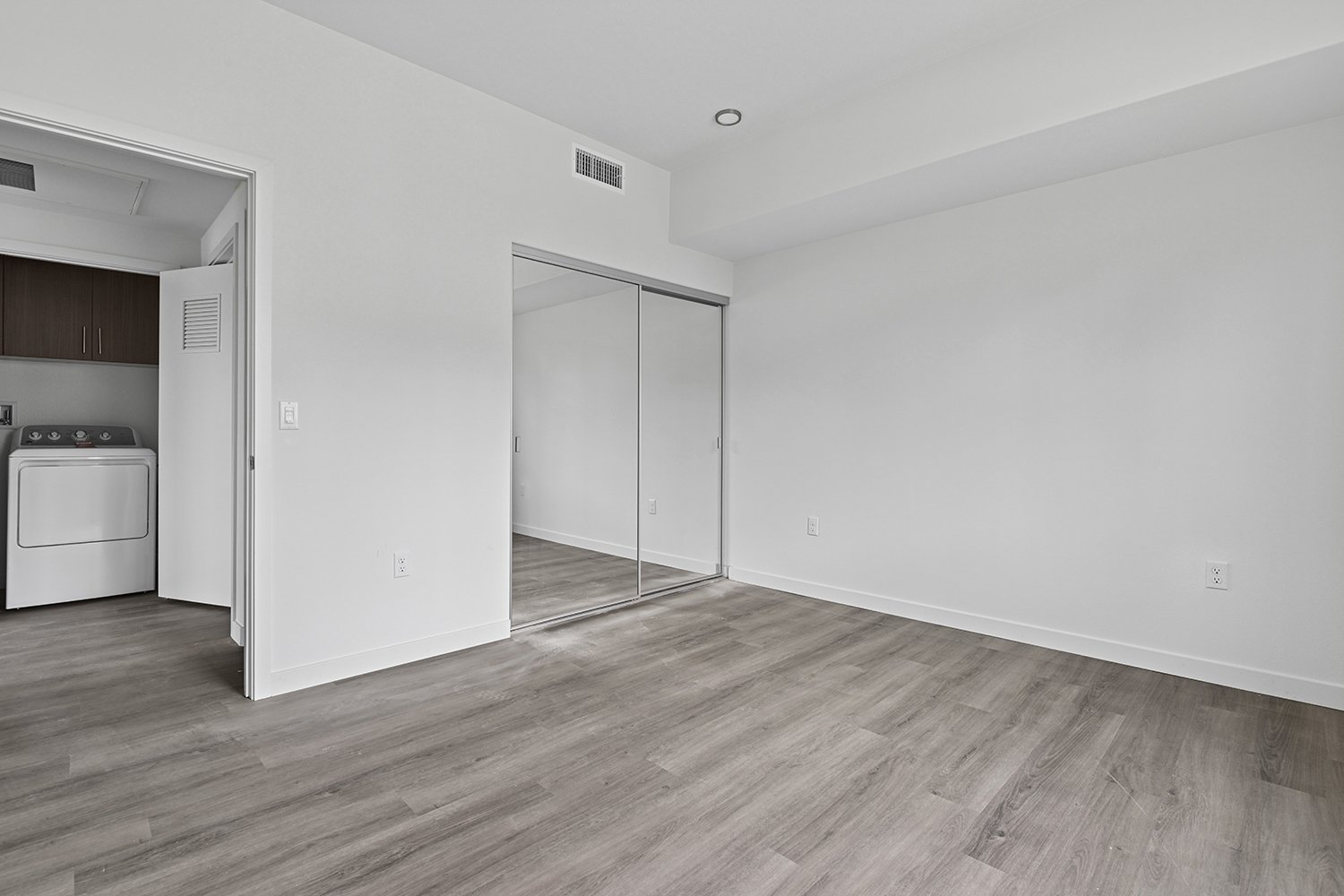 Gorgeous bedroom in Rendezvous Phase II apartments with wood-style plank flooring, spacious closet, and floor to ceiling windows with decorative Juliet balcony for charm and luxury. 