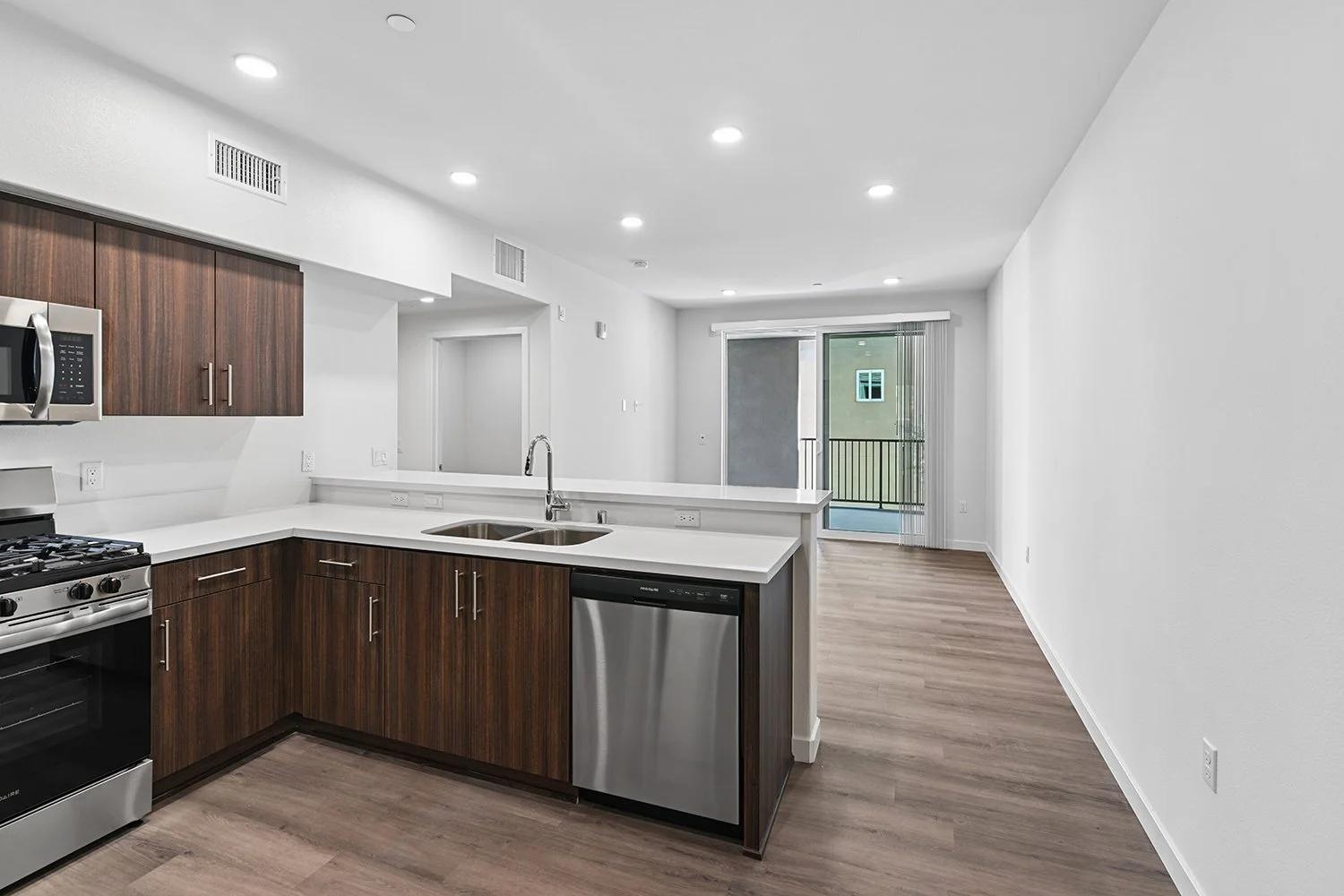 Kitchen in Rendezvous Phase II apartment home with plank flooring, stainless appliances, quartz countertops, and a large breakfast bar overlooking the living area and doors leading to private patio. 